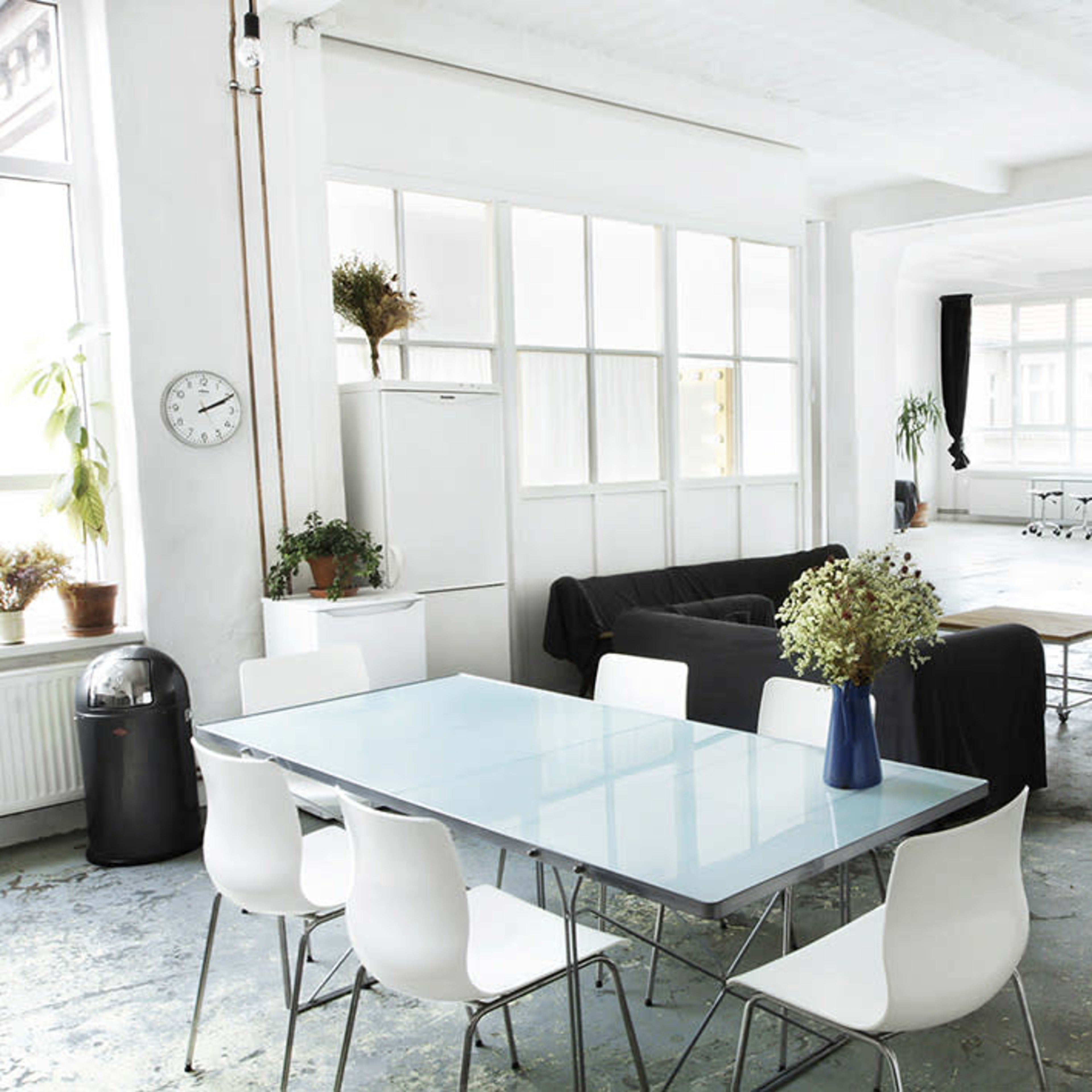 A spacious, modern room featuring a dining table with chairs, a black couch, and large windows providing ample natural light.