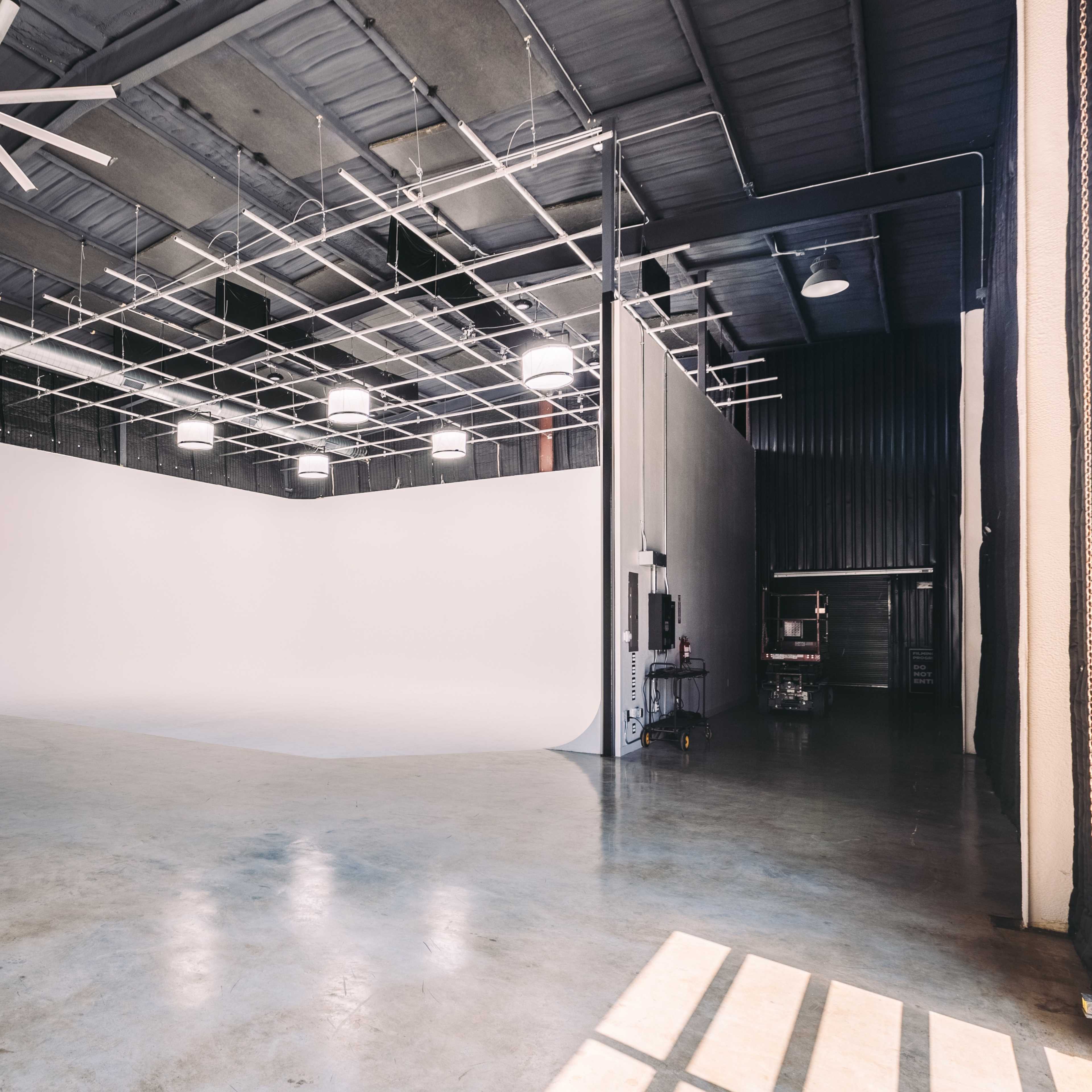 A large, empty studio space with a seamless white backdrop and concrete flooring.