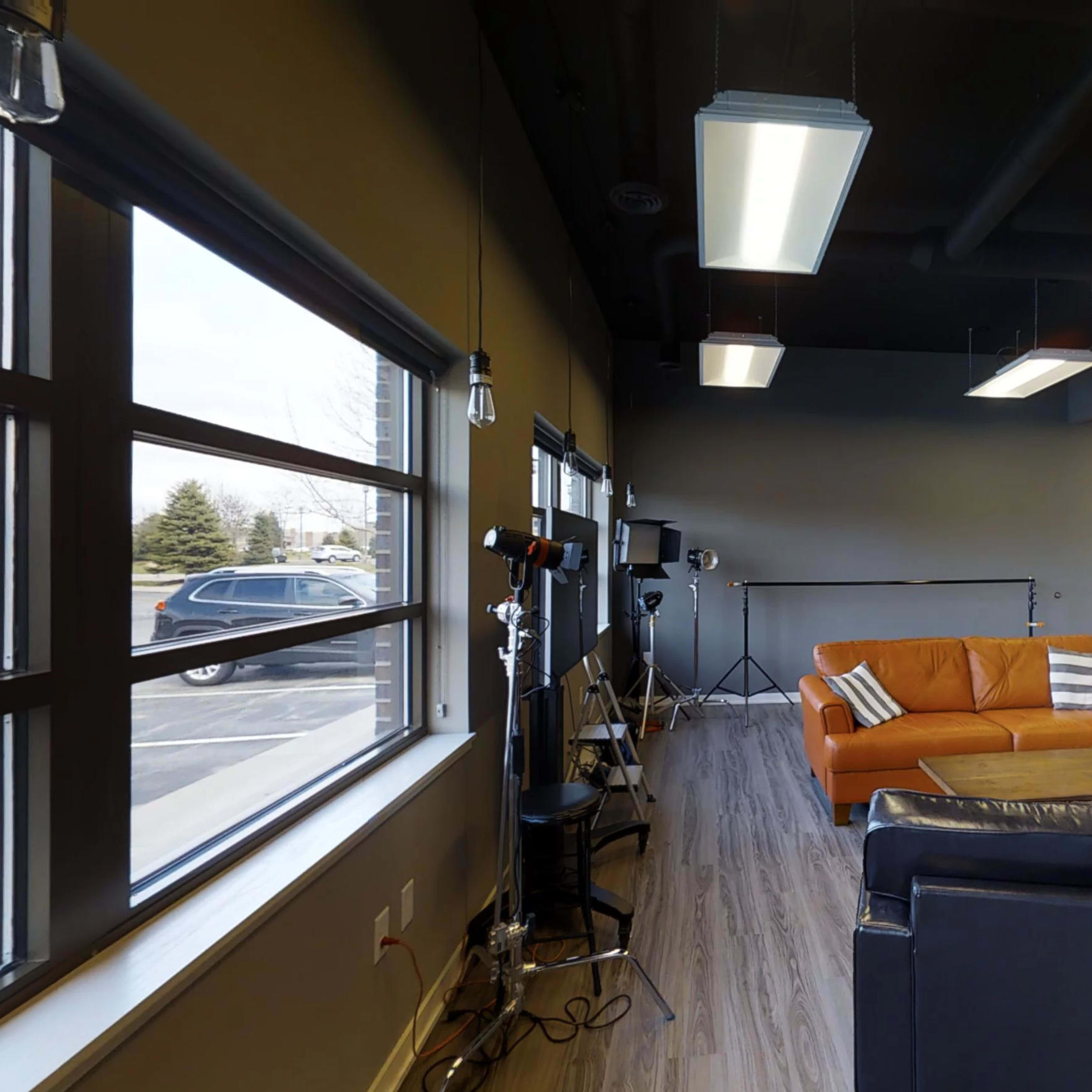 A modern interior of a lounge area featuring a brown sofa, a black armchair, and studio lighting equipment.