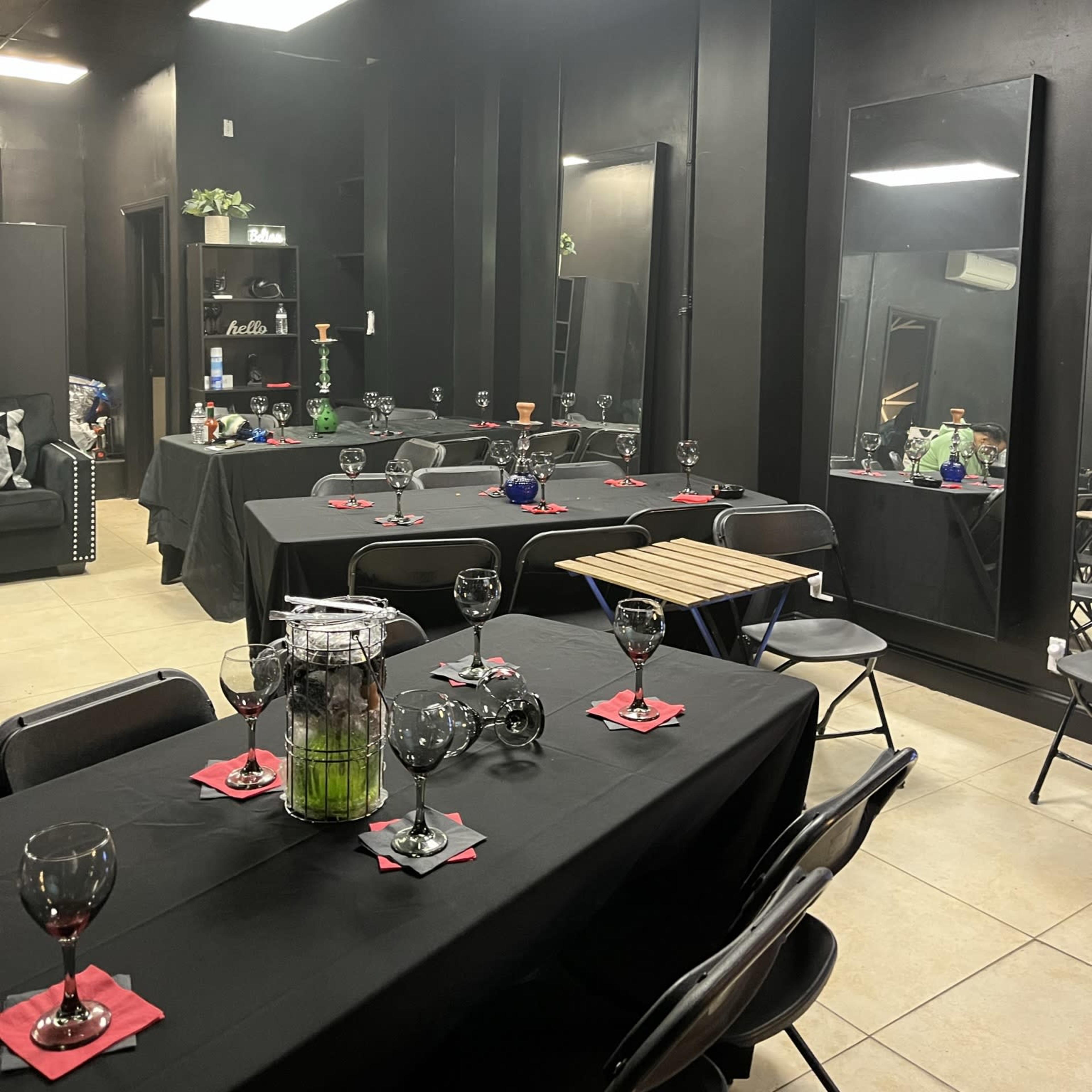 A dimly lit black room with several tables set for an event, featuring black tablecloths and glassware.