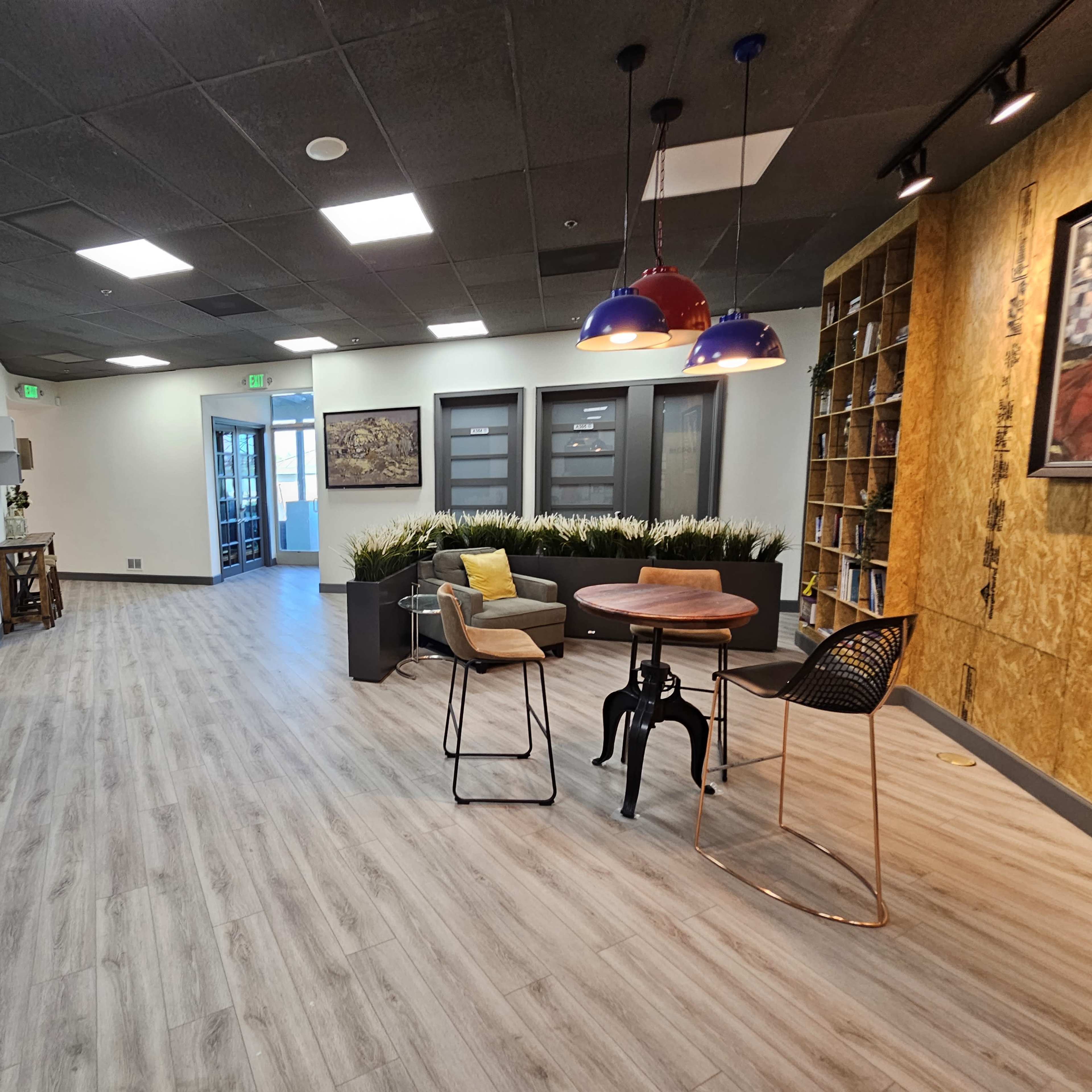 A modern office lobby with sleek flooring, a seating area featuring a round table and chairs, and large windows leading to an adjacent room.