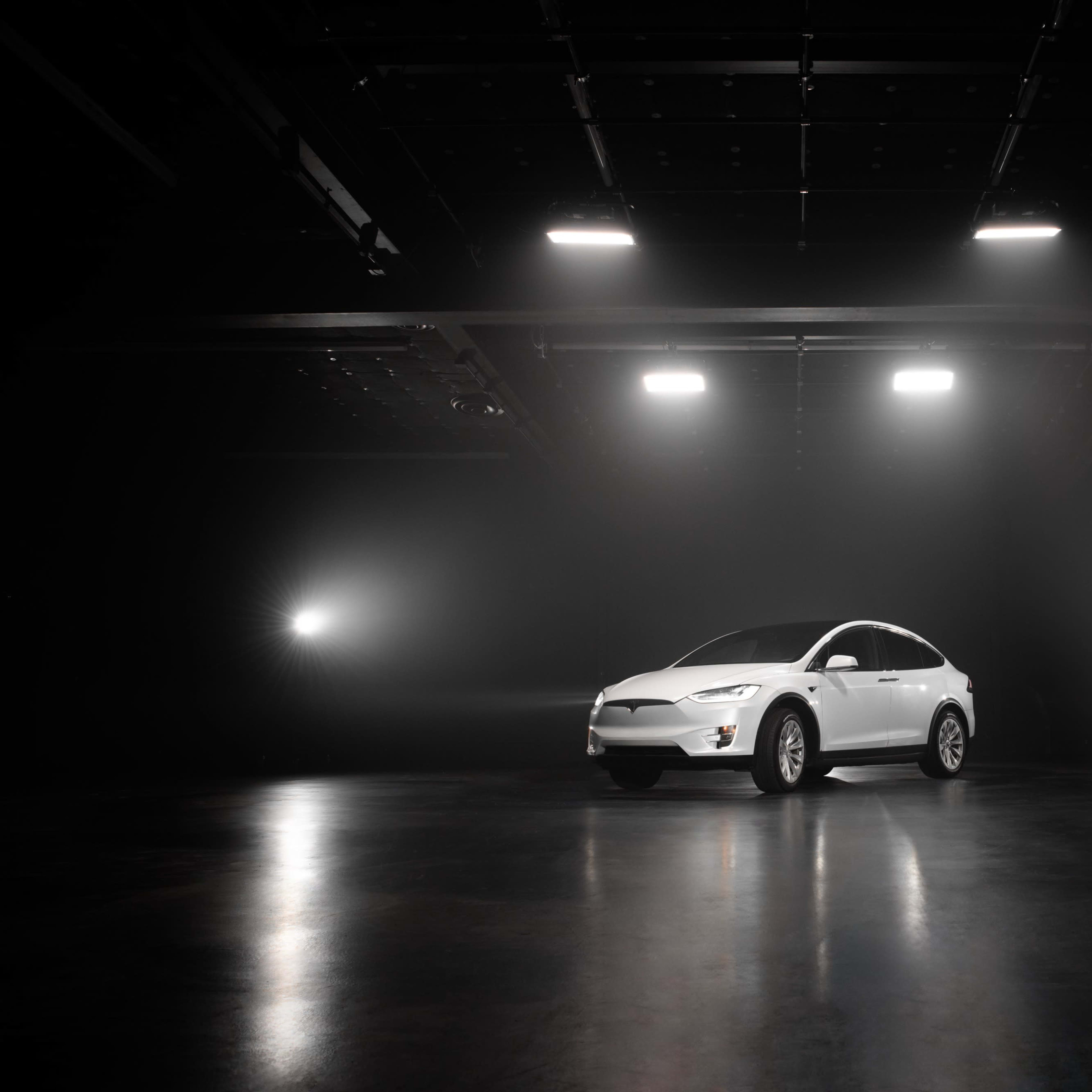 A white car is positioned in a dimly lit studio with bright lights shining from above.