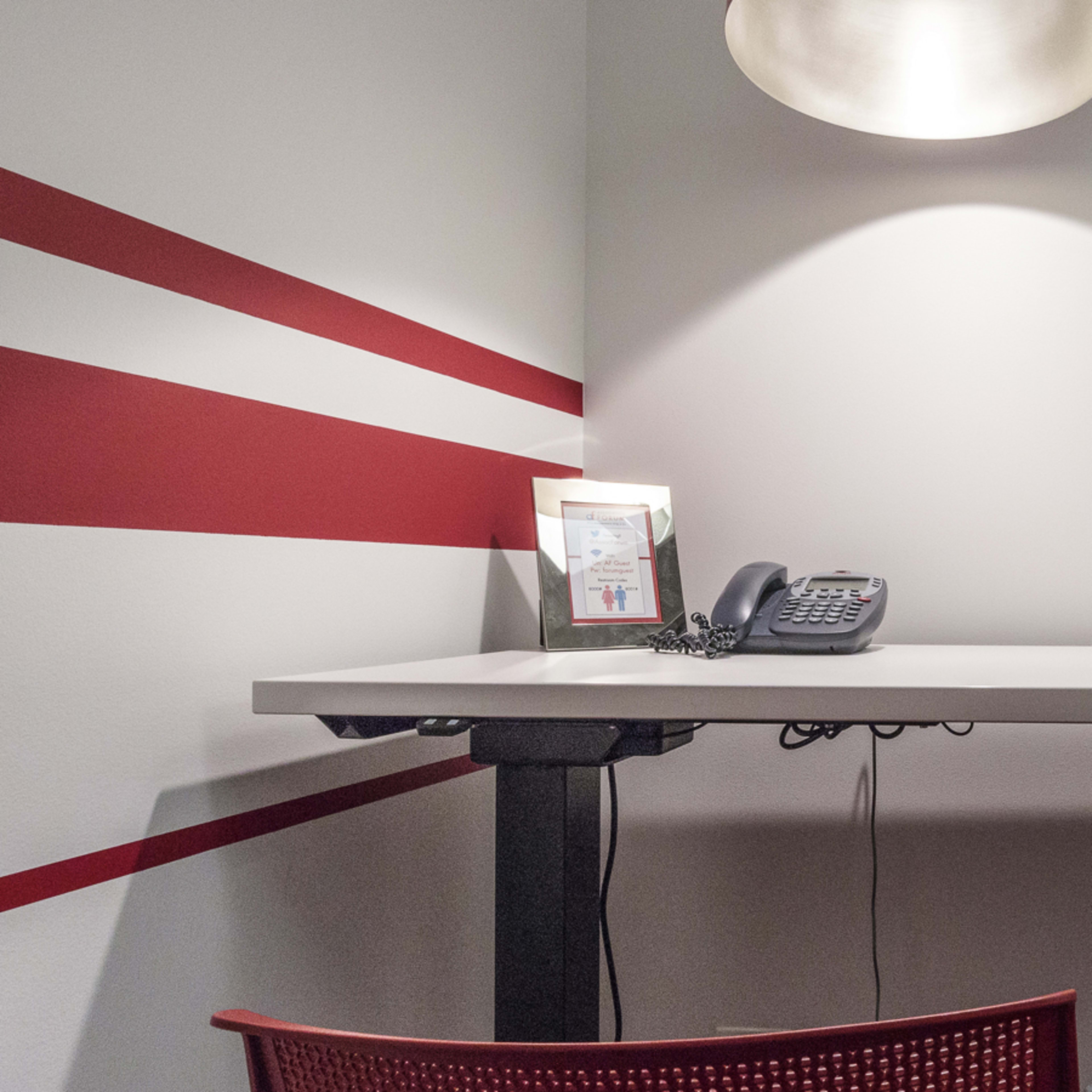 A modern desk with a phone and a framed item is positioned against a wall featuring red stripes.