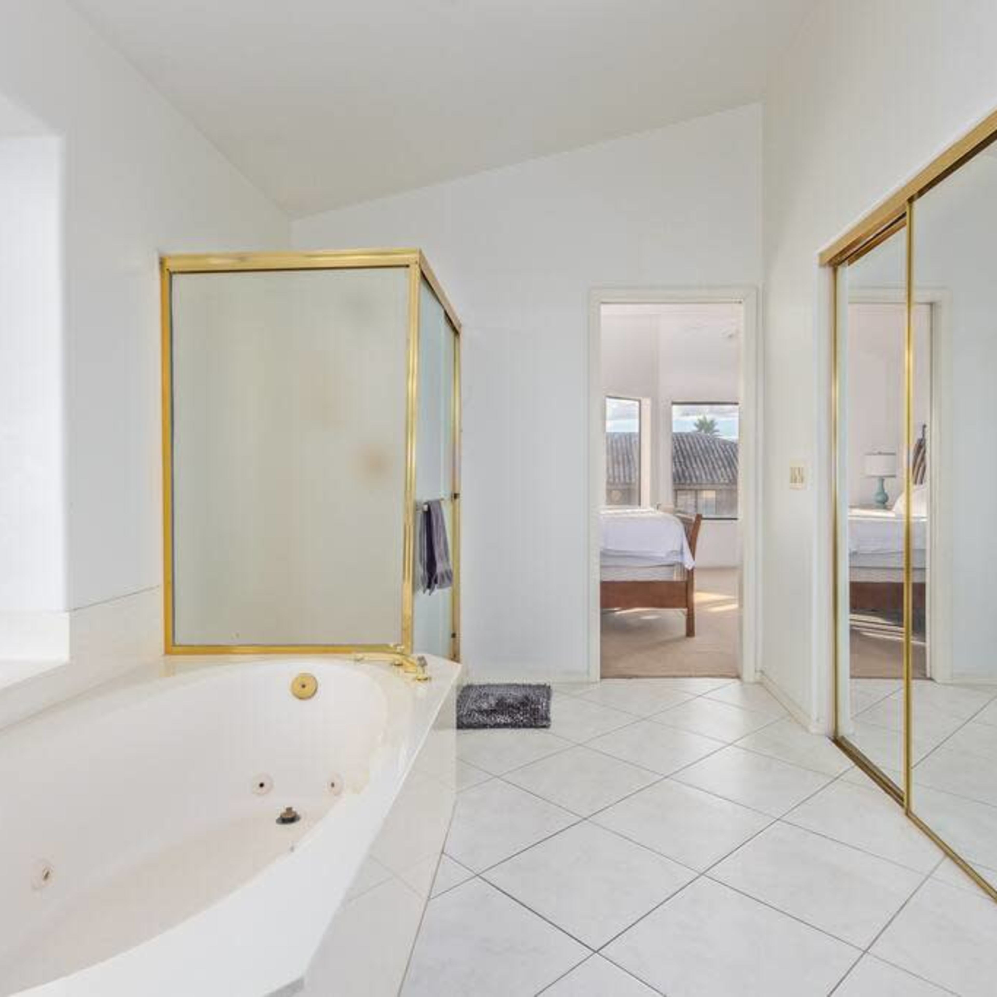 A bathroom with a glass shower enclosure, a large bathtub, and a mirrored closet door, all set in a bright, minimalist space.