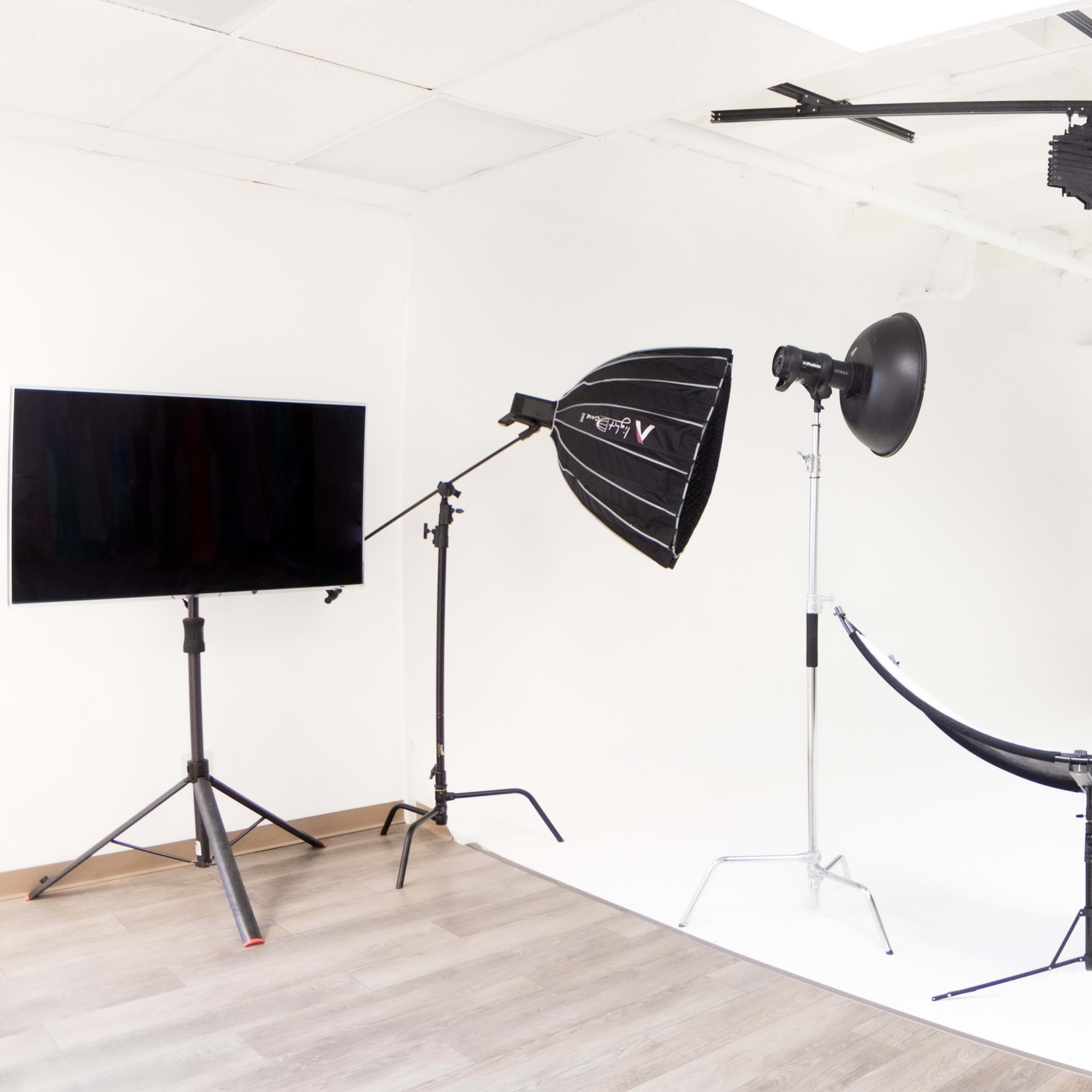 A photography studio is equipped with various lighting setups and a stool in the center of a white backdrop.