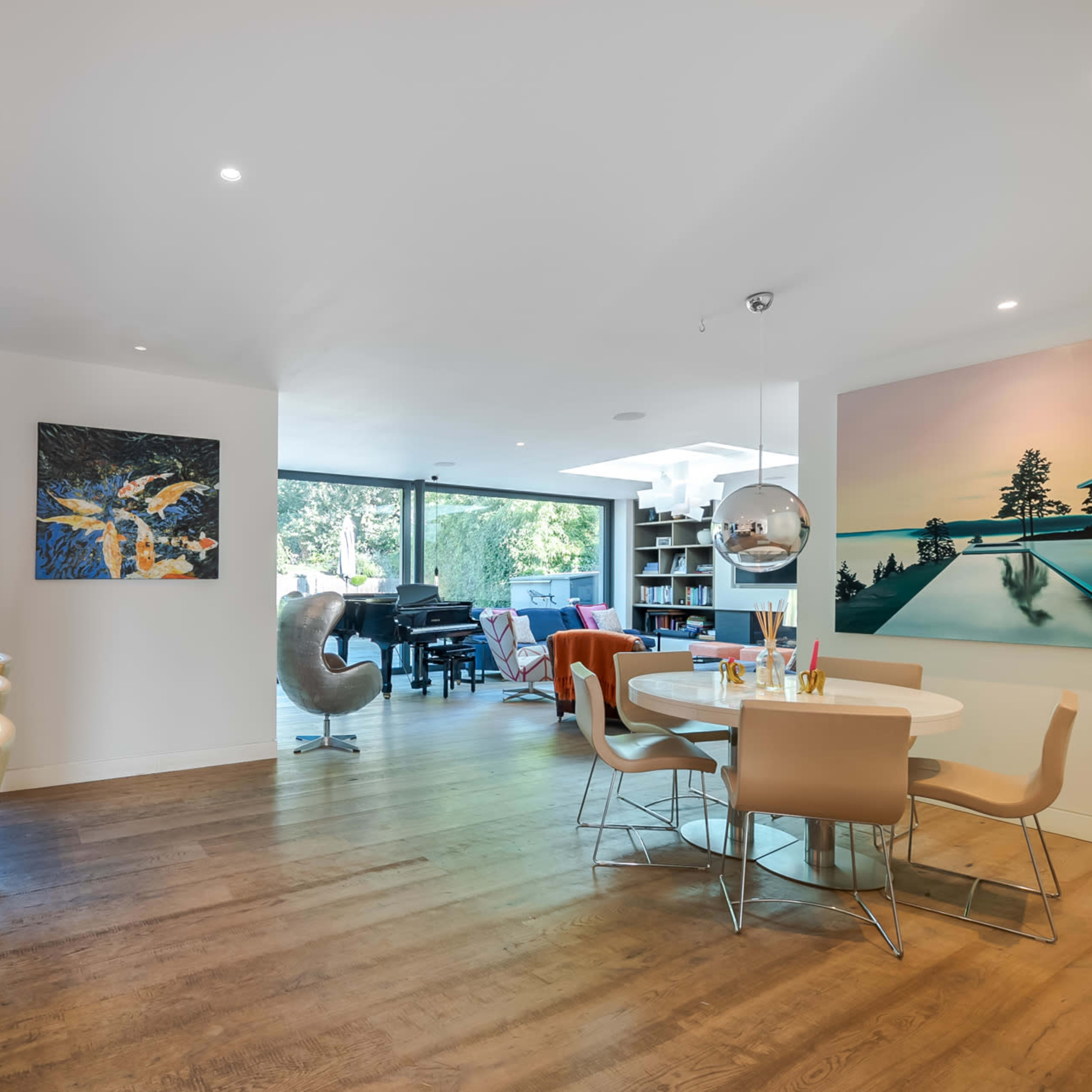 A modern living space featuring a kitchen island, a dining area with a round table, and large windows that provide natural light.