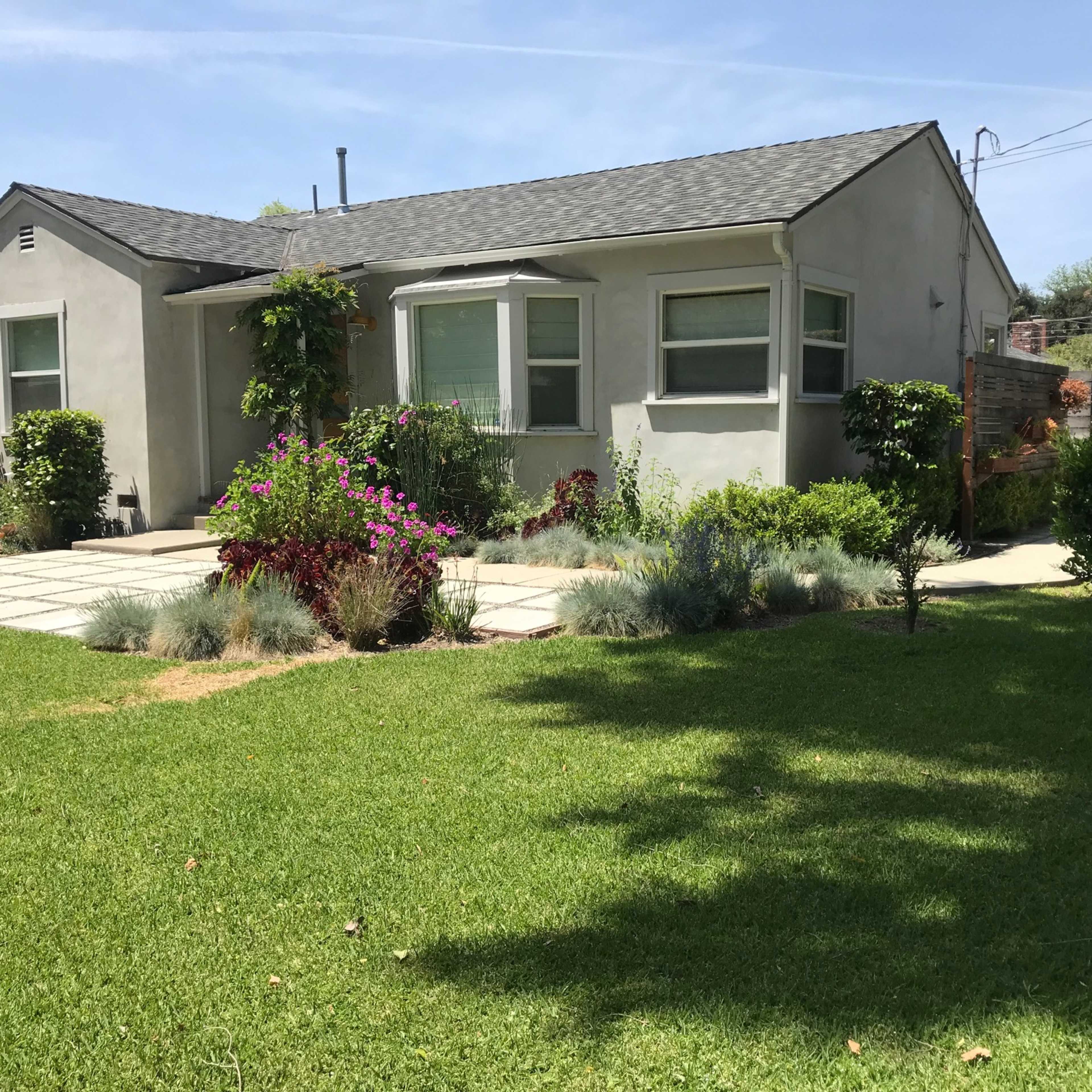 A single-story house with a gray exterior and manicured front yard featuring a variety of flowers and shrubs.