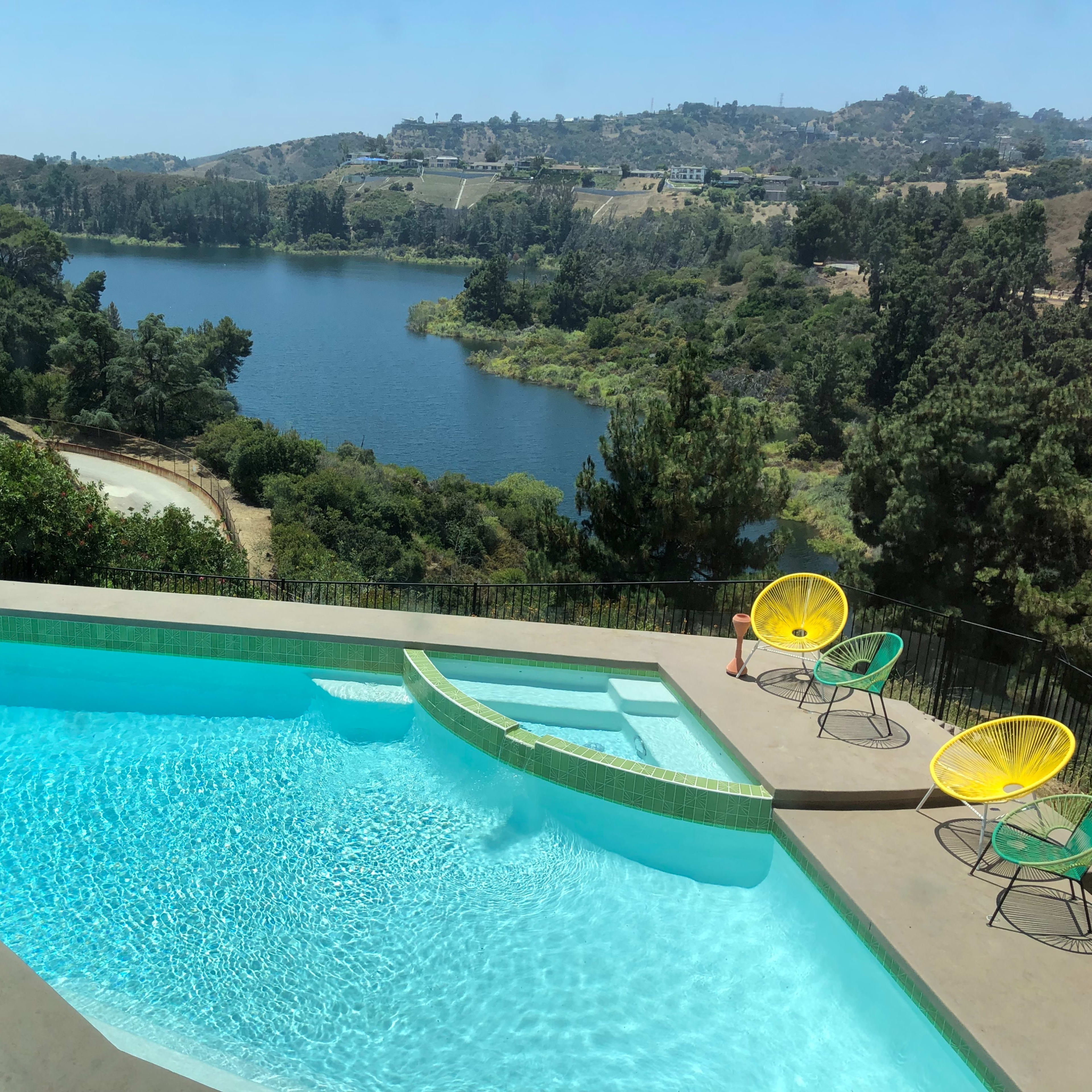 A swimming pool overlooks a calm lake surrounded by greenery and hillside.