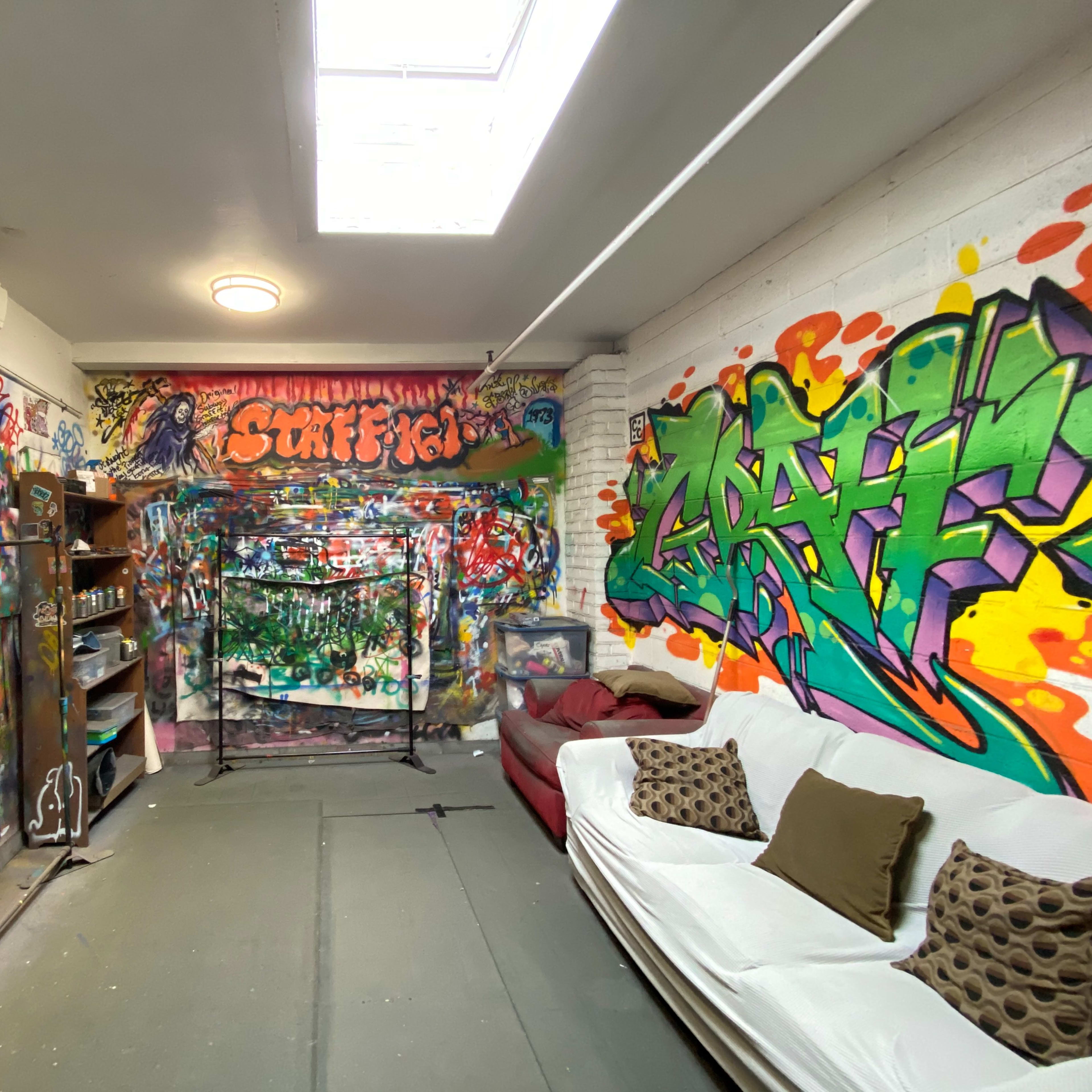 A colorful graffiti-covered room with a couch, shelves, and a backdrop for creative activities.