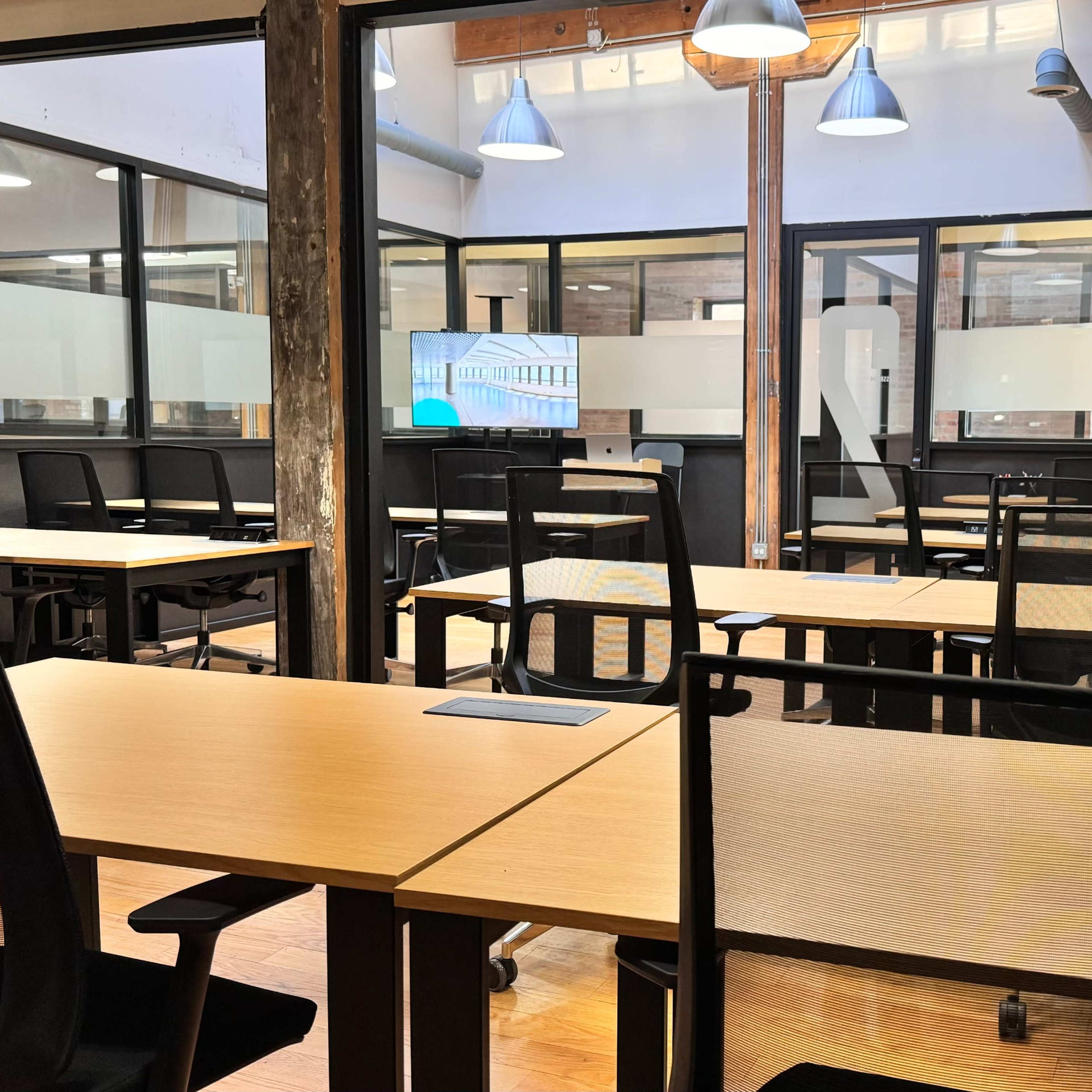 An interior of a modern office space featuring several empty desks arranged neatly in a well-lit room with large windows.