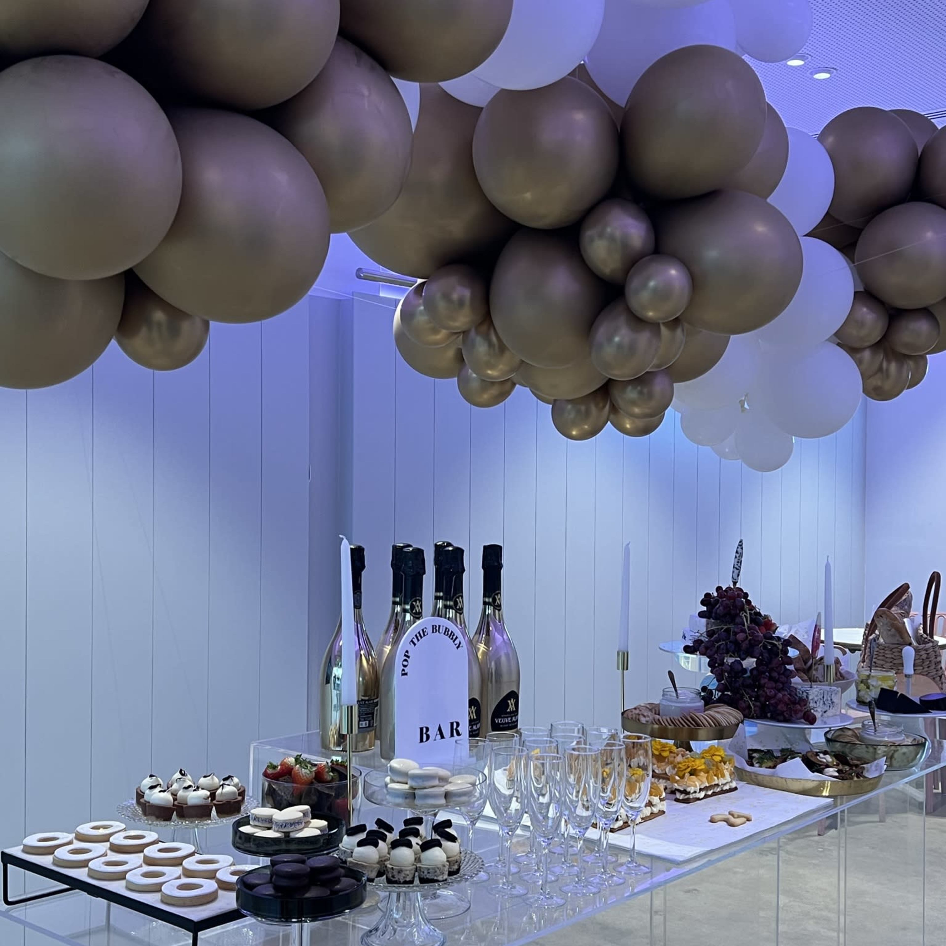 A party setup with a table featuring an array of desserts and drinks, topped with decorative balloons.