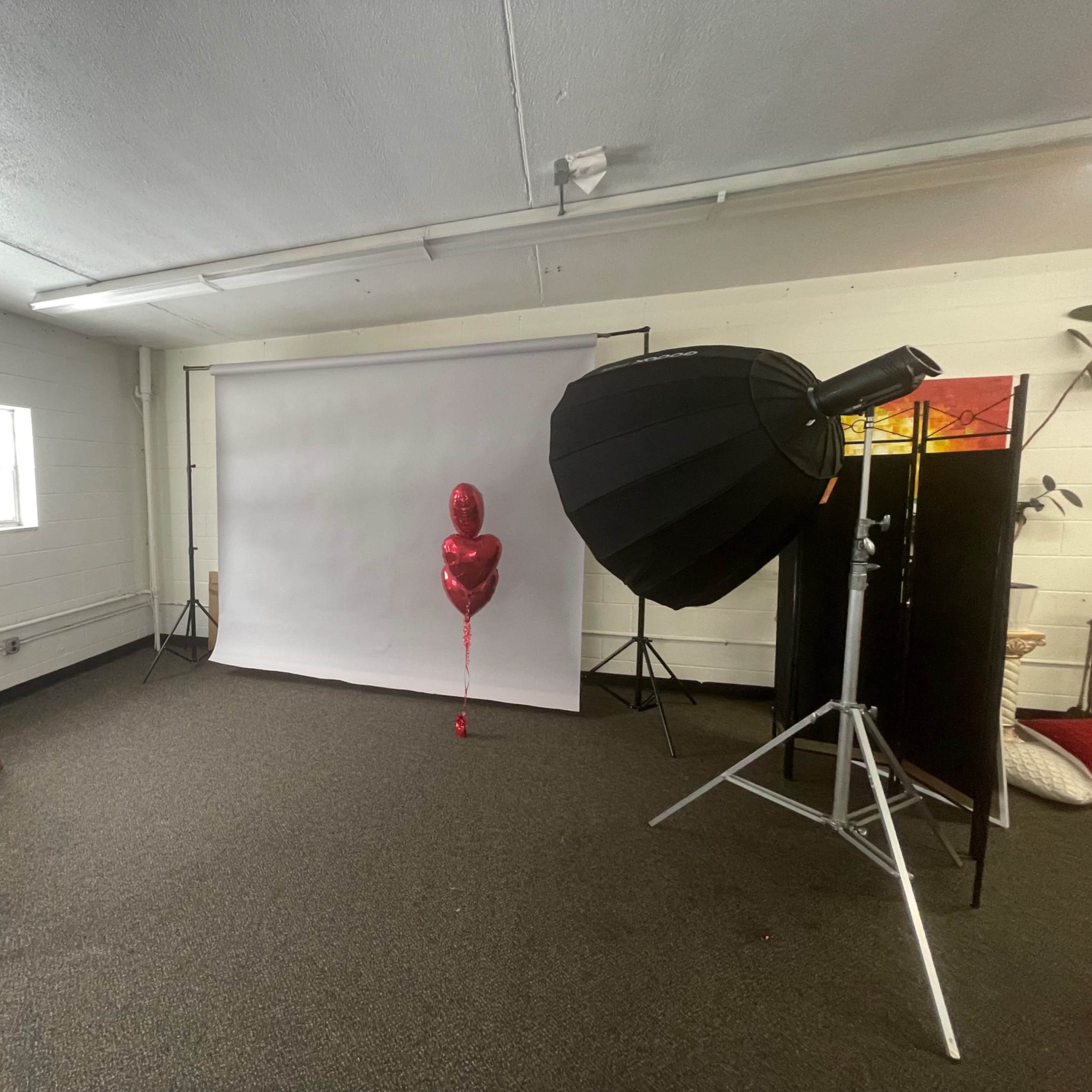 A photography studio is set up with a backdrop, lighting equipment, a ladder, and a single red balloon on a stand.