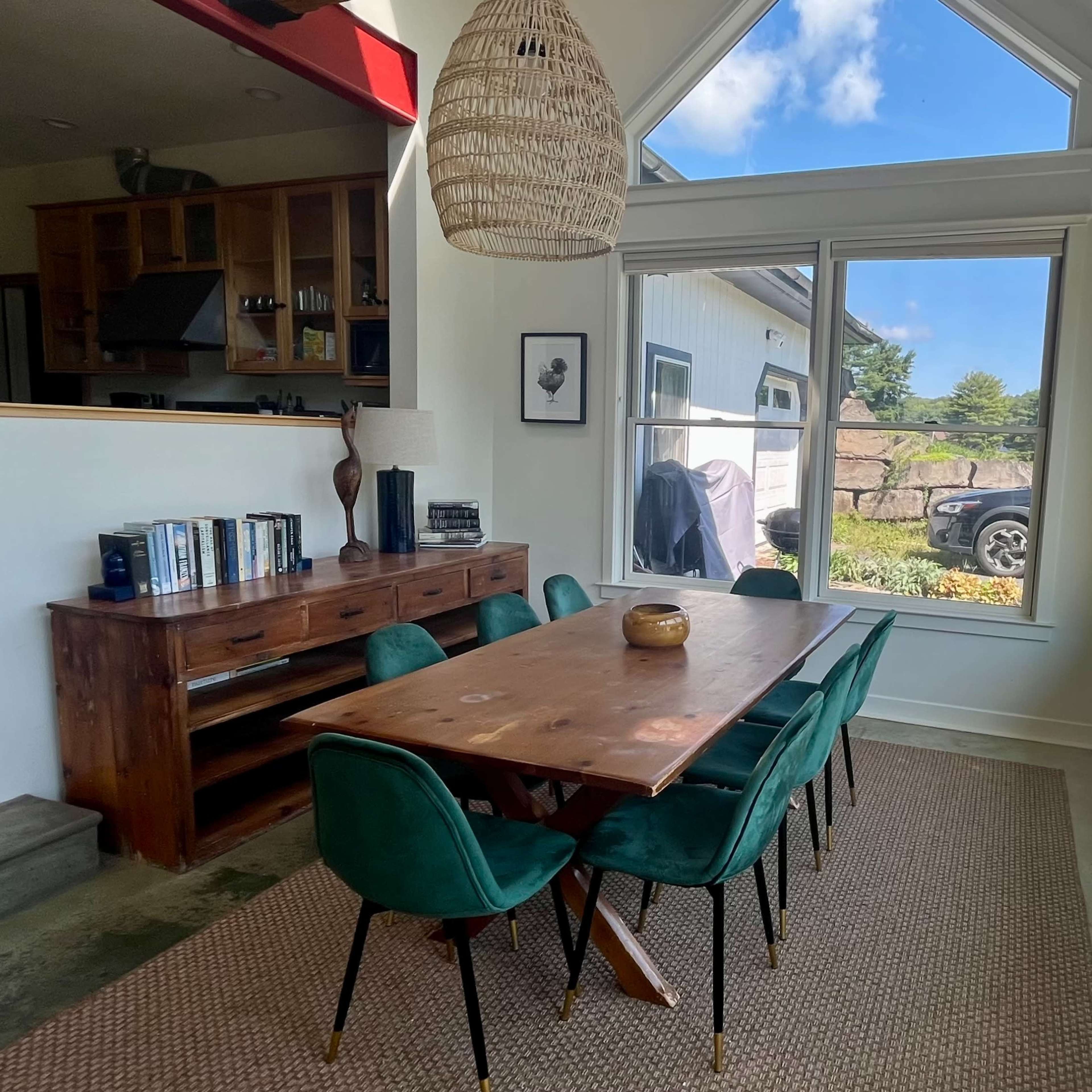 A dining area features a wooden table surrounded by green chairs, with large windows allowing natural light to fill the space.