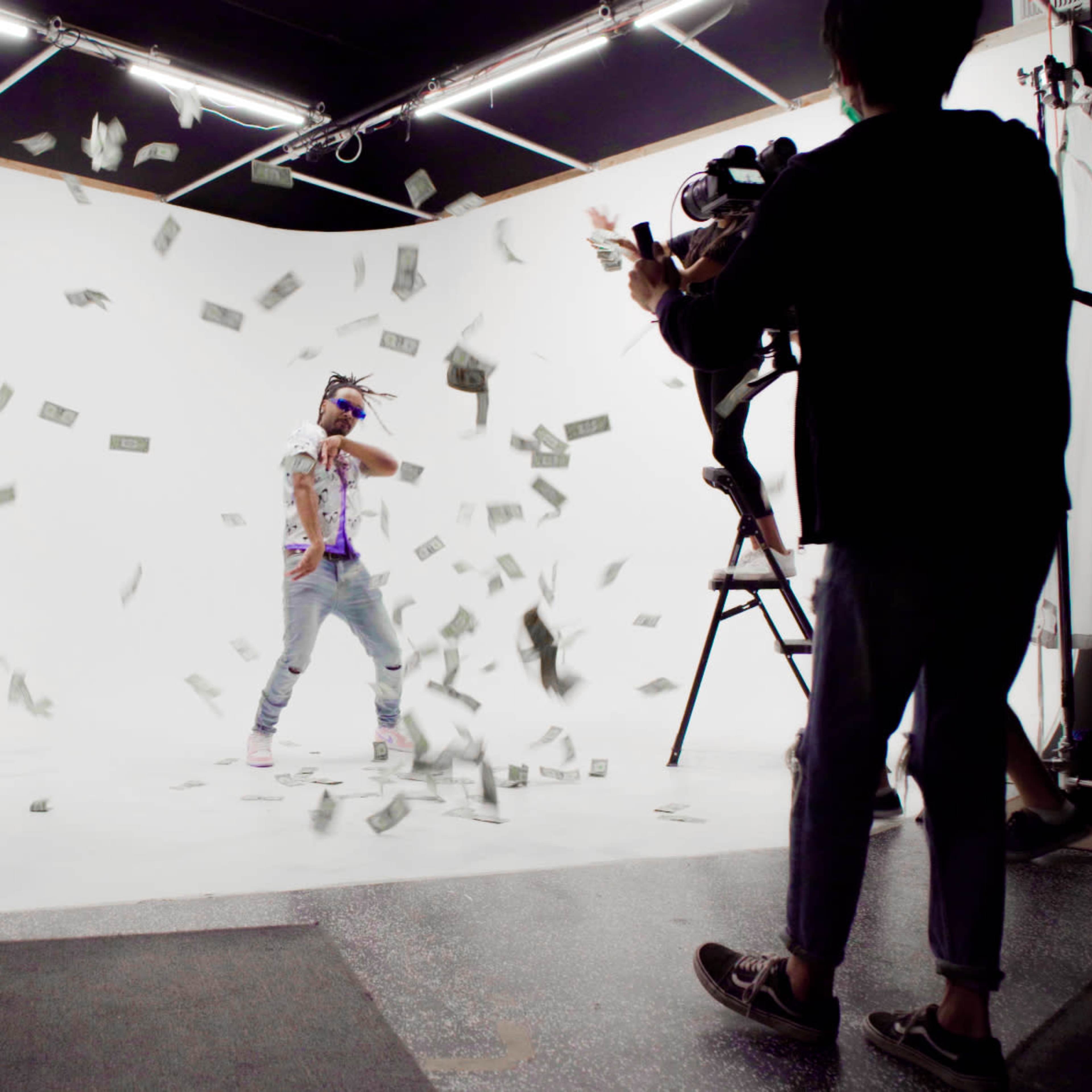 A group of people captures a scene with a person standing amidst falling dollar bills on a film set.
