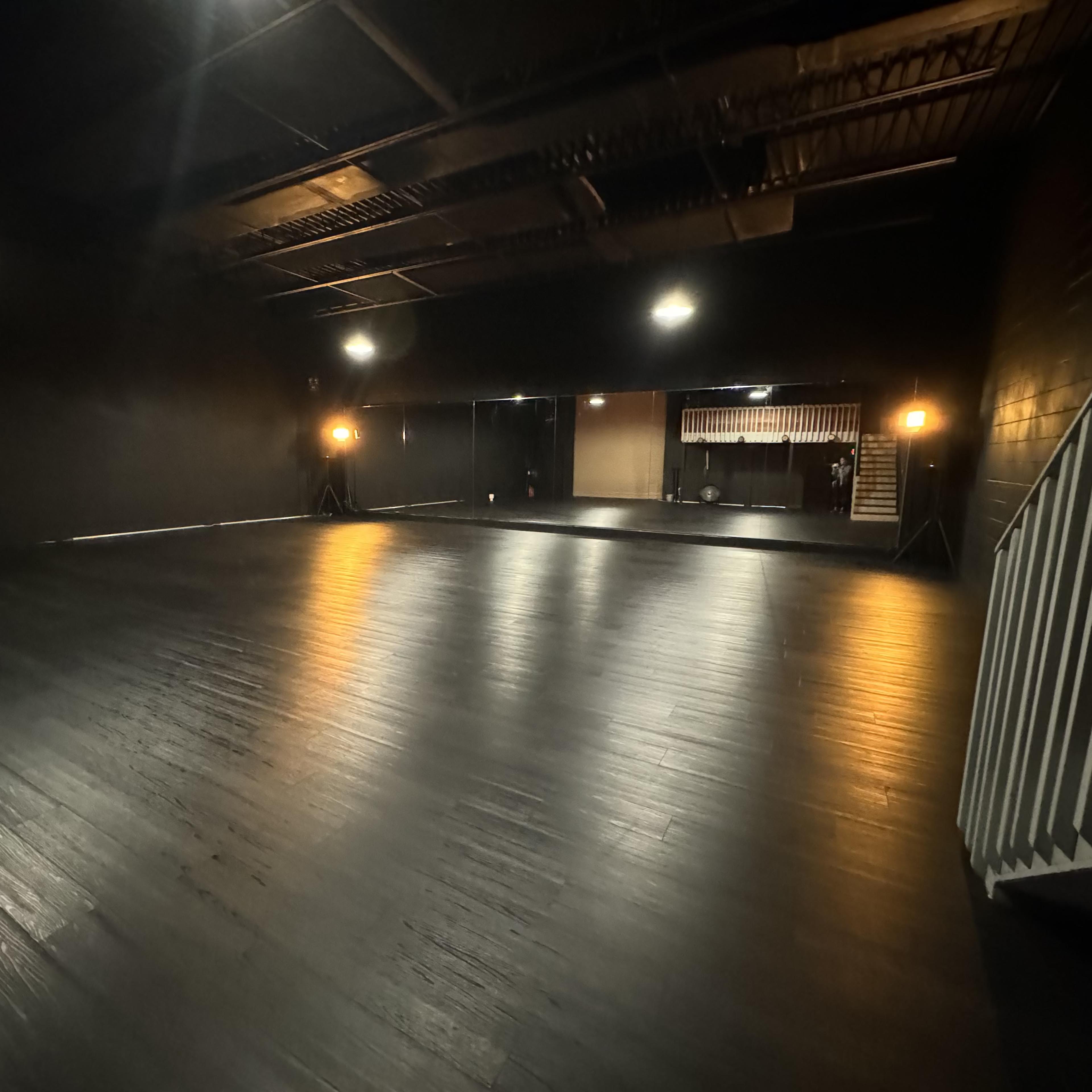 A large, empty black-walled studio space with a polished wooden floor and dim lighting.
