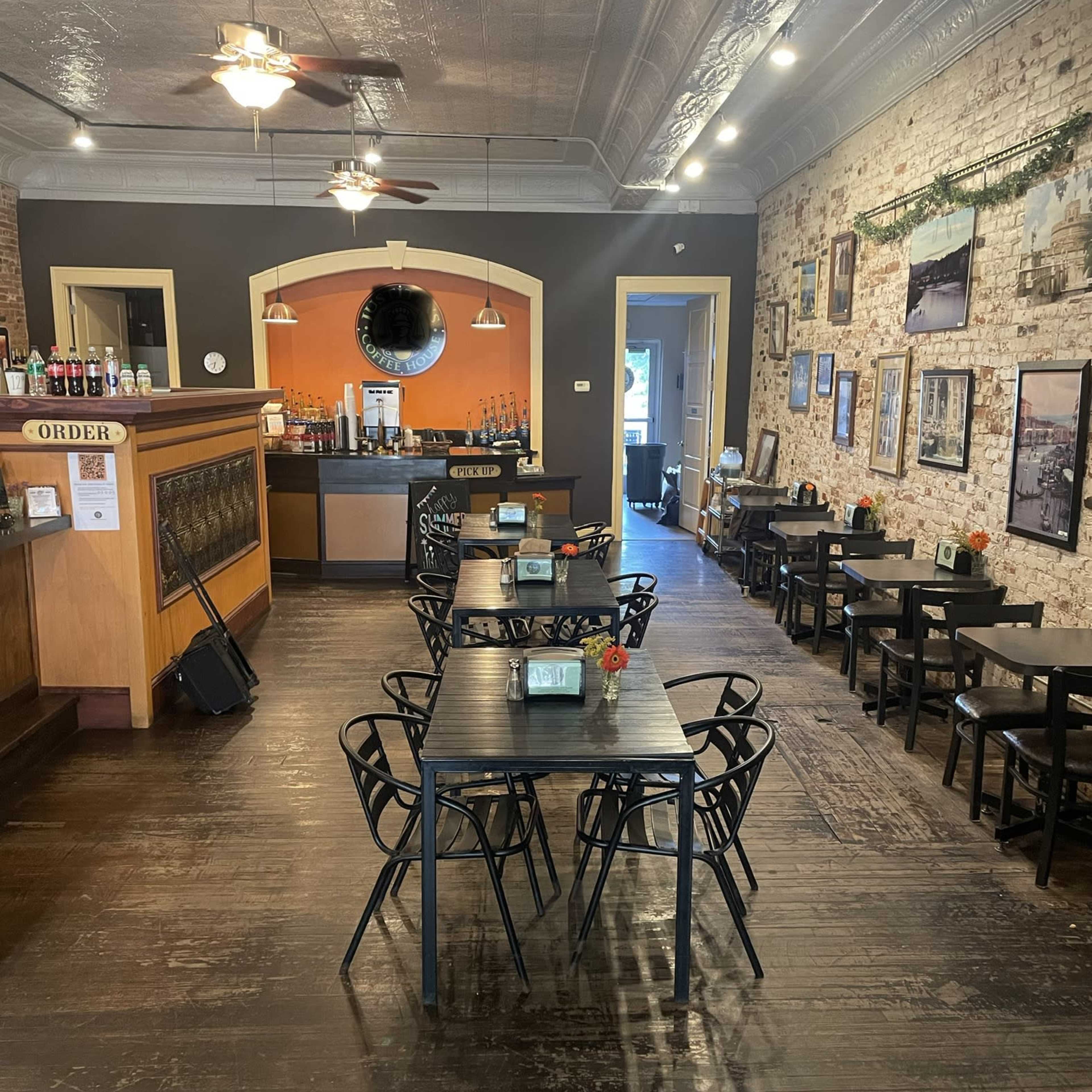 A spacious café with wooden floors, tables arranged for dining, and a counter in the back area.