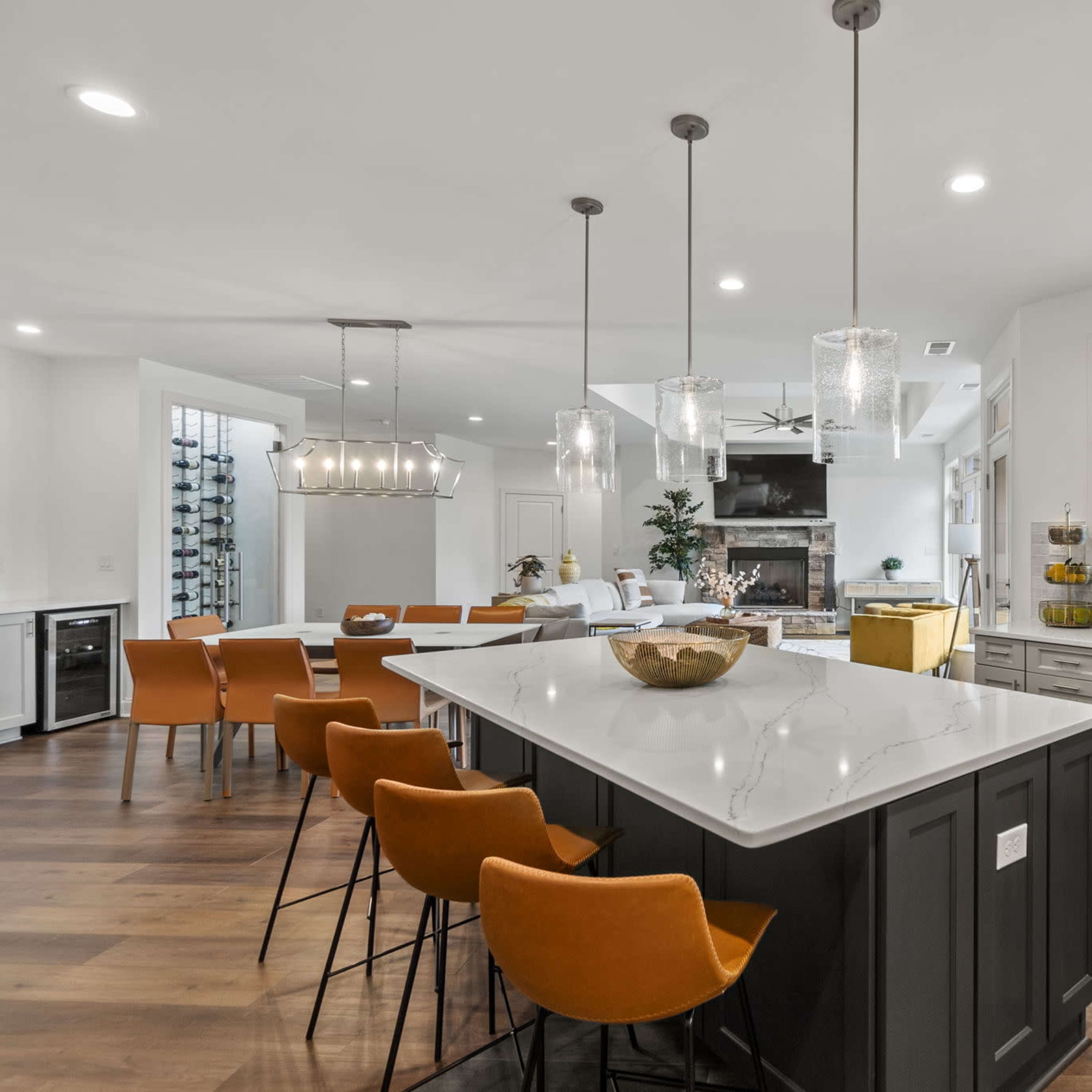 A modern kitchen features a large island with seating, pendant lights, and a dining area, all set against a backdrop of wooden flooring and white cabinetry.