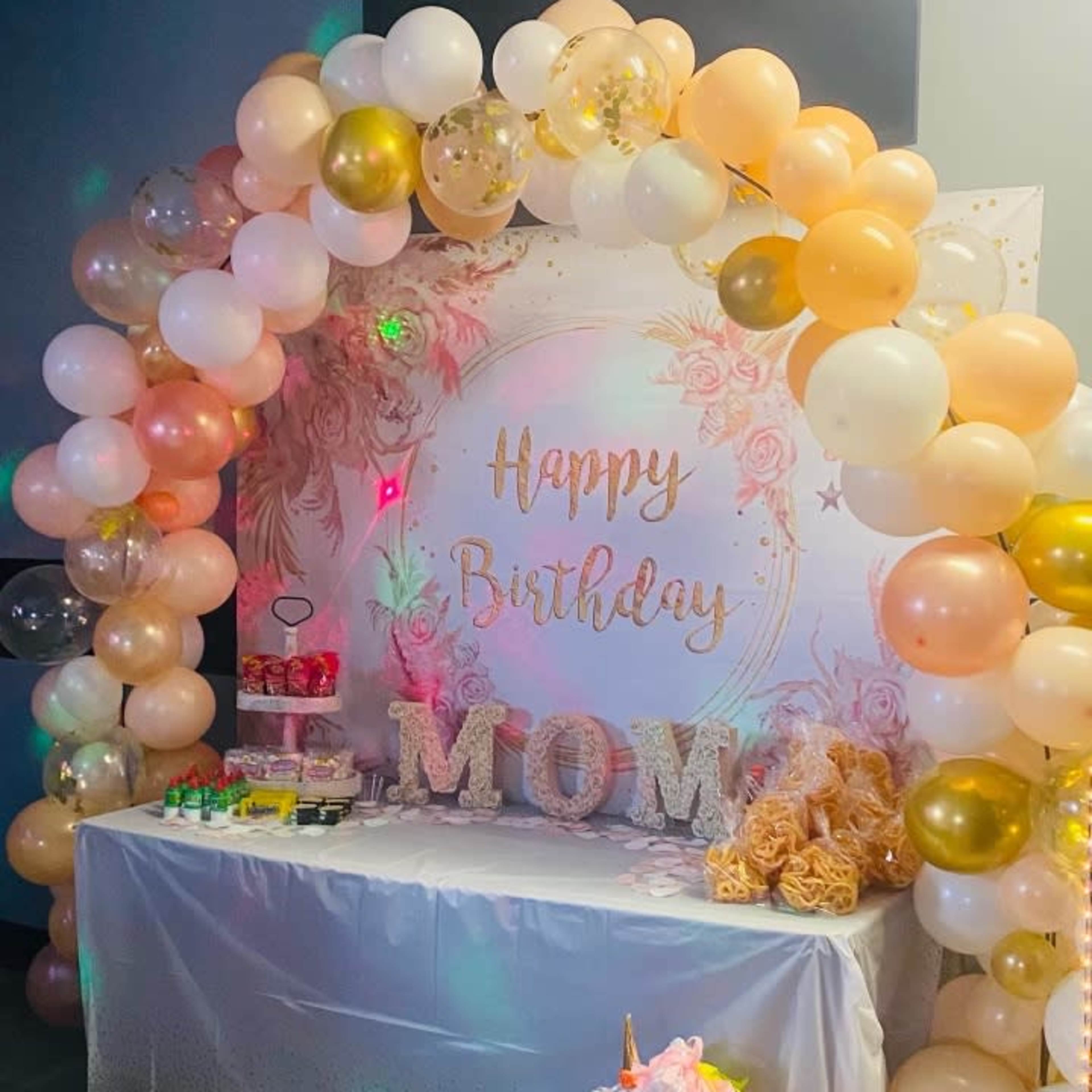 A birthday celebration display features a decorated table with a "Happy Birthday MOM" backdrop, adorned with balloons and a unicorn figure.