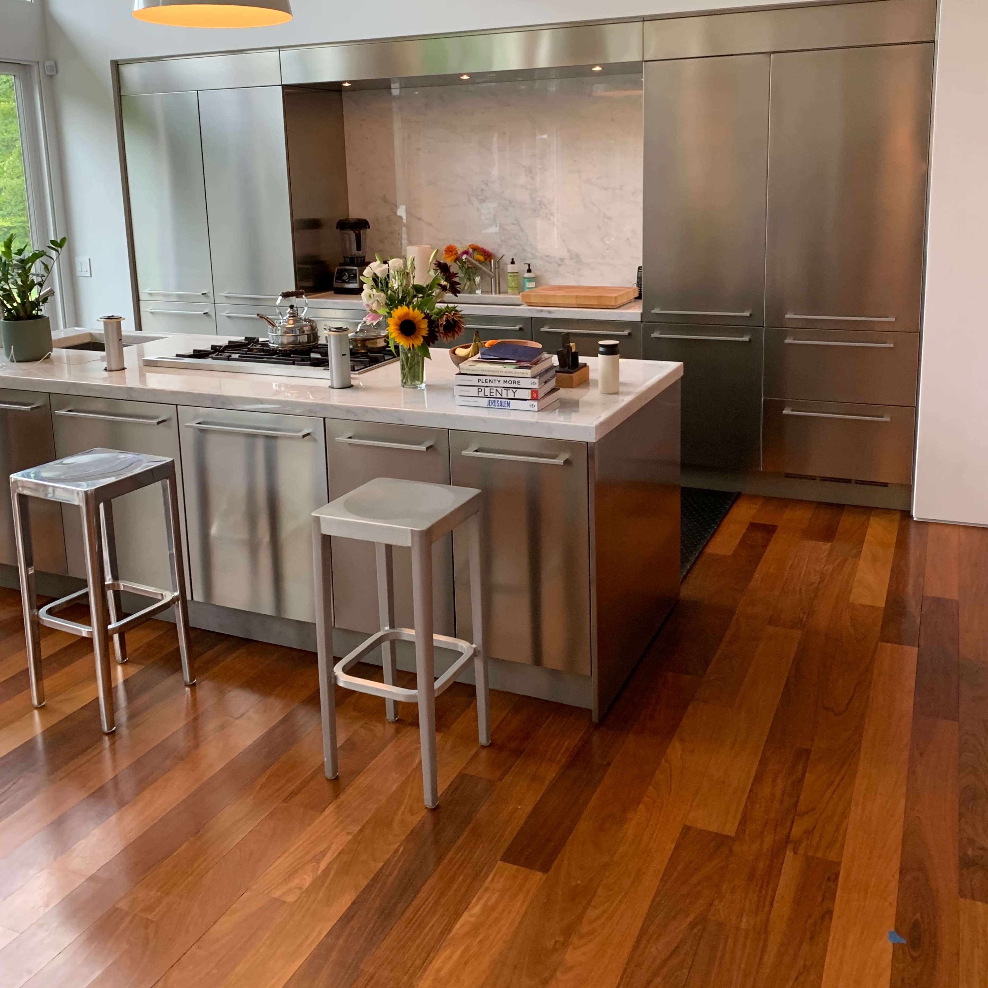 A modern kitchen with stainless steel cabinets and appliances, a central island, and a wooden floor.