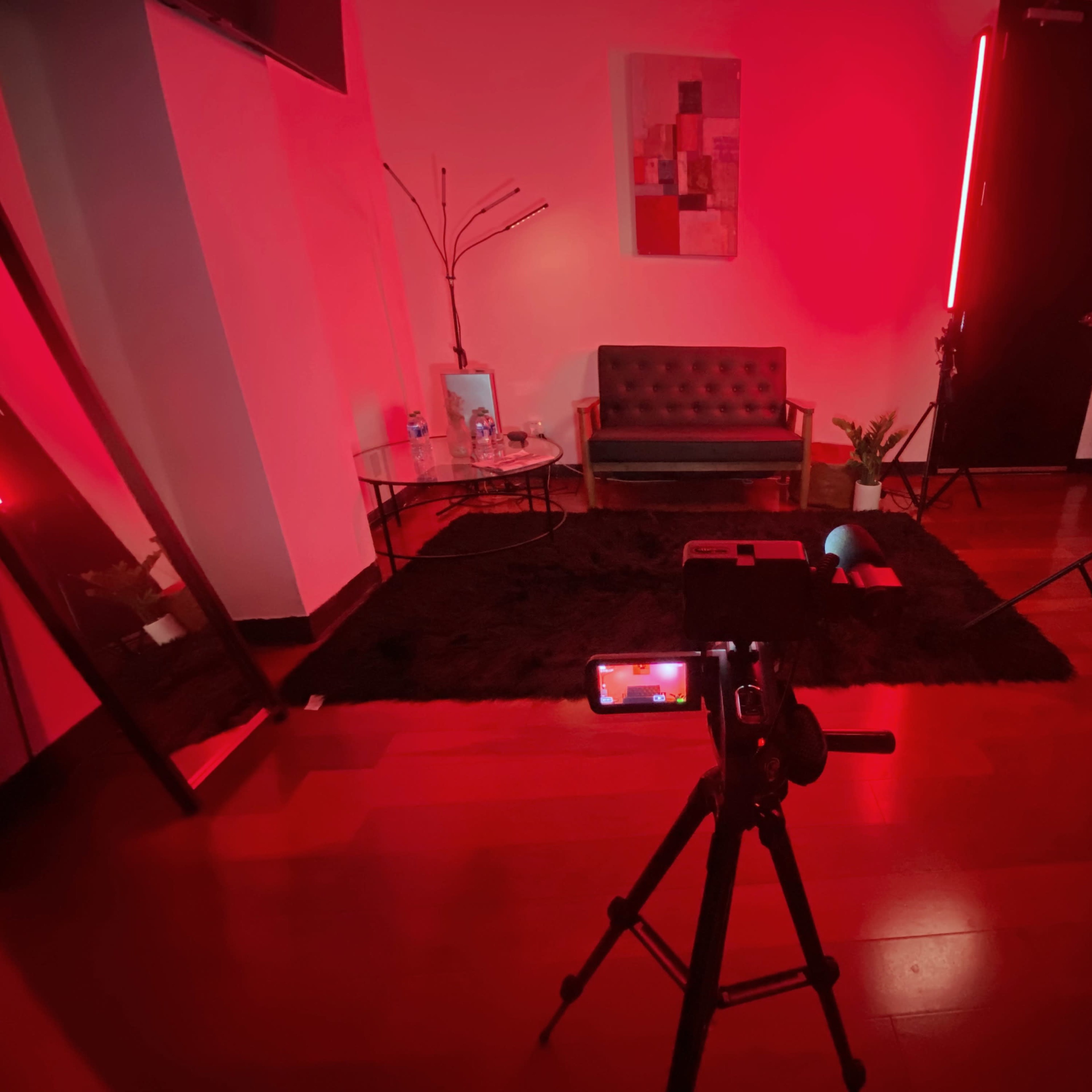 The scene features a dimly lit room with a couch, a small table, and a camera on a tripod facing the setup.