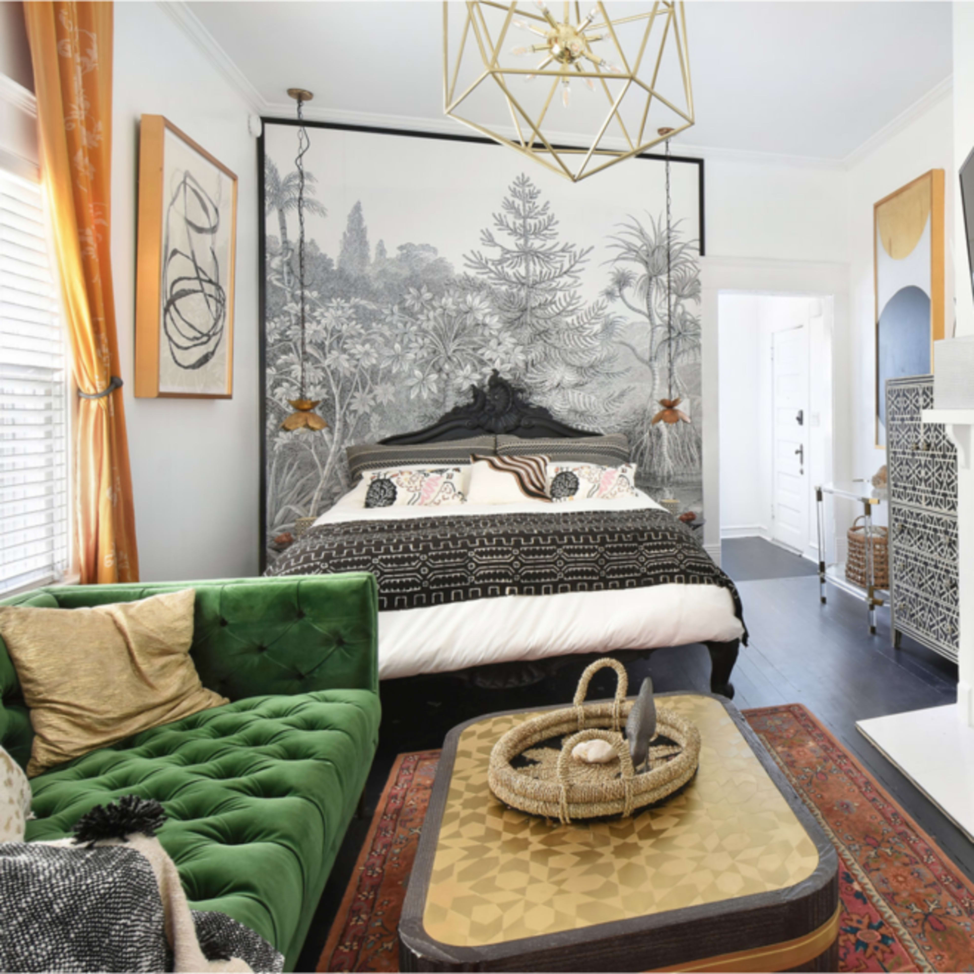 A stylish bedroom with a green velvet sofa, a large bed, and a decorative fireplace, complemented by a patterned wall mural and modern lighting fixtures.