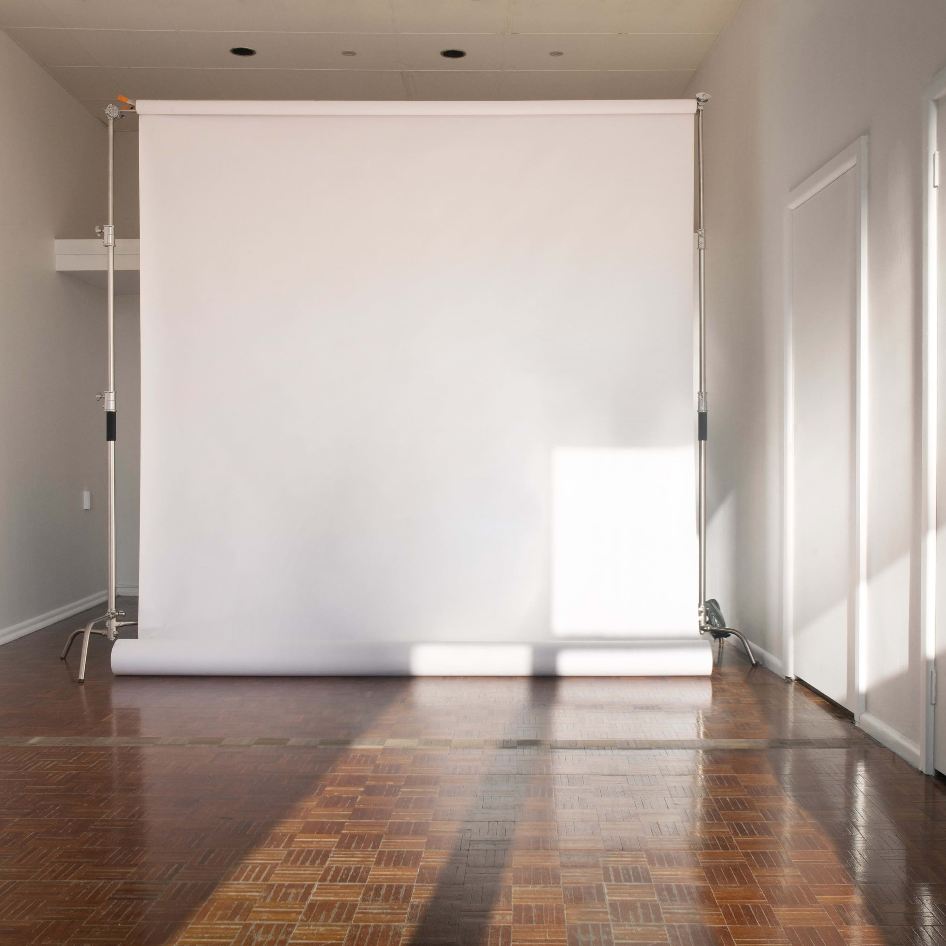 A minimalist studio space with a white backdrop roll, wooden flooring, and two closed doors on adjacent walls.