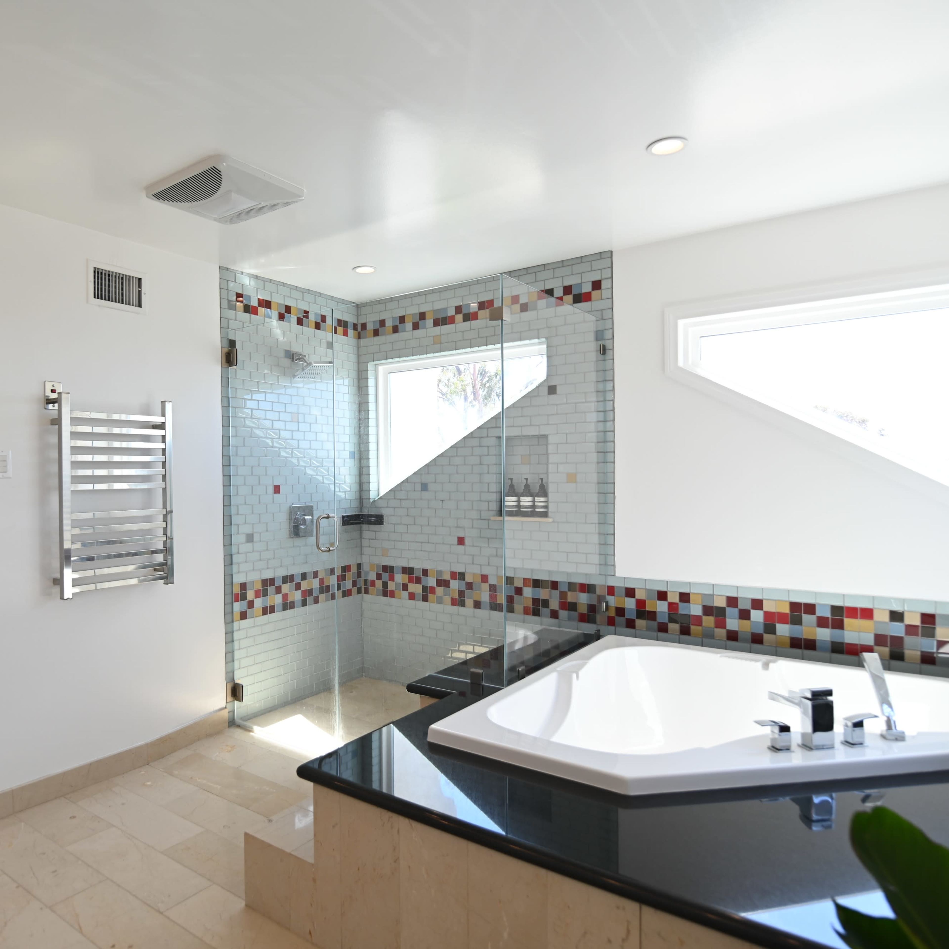 A modern bathroom featuring a corner bathtub, a glass shower enclosure, and tiled walls with colorful accents.