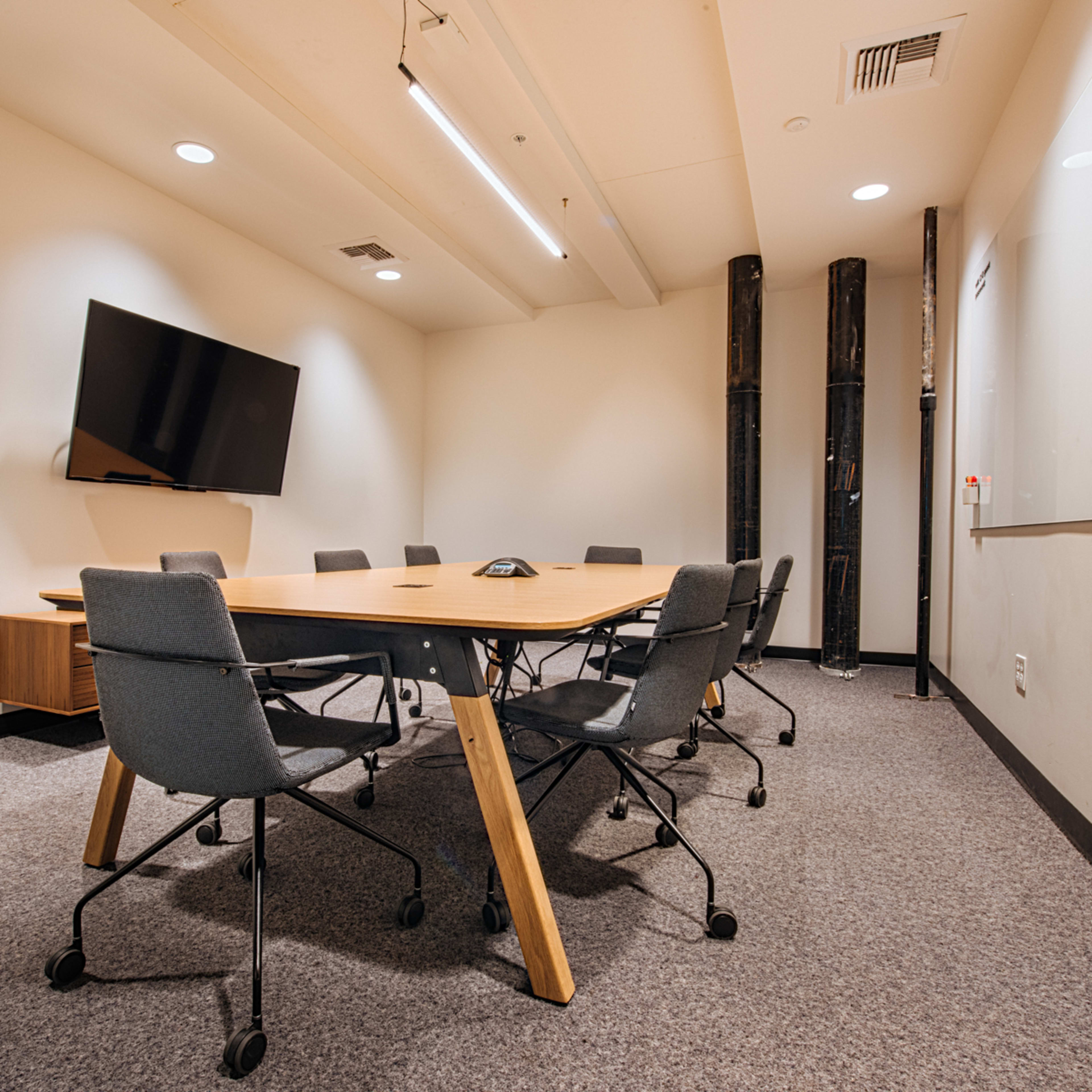 A conference room featuring a large table surrounded by chairs, a television on the wall, and a plant in a pot.