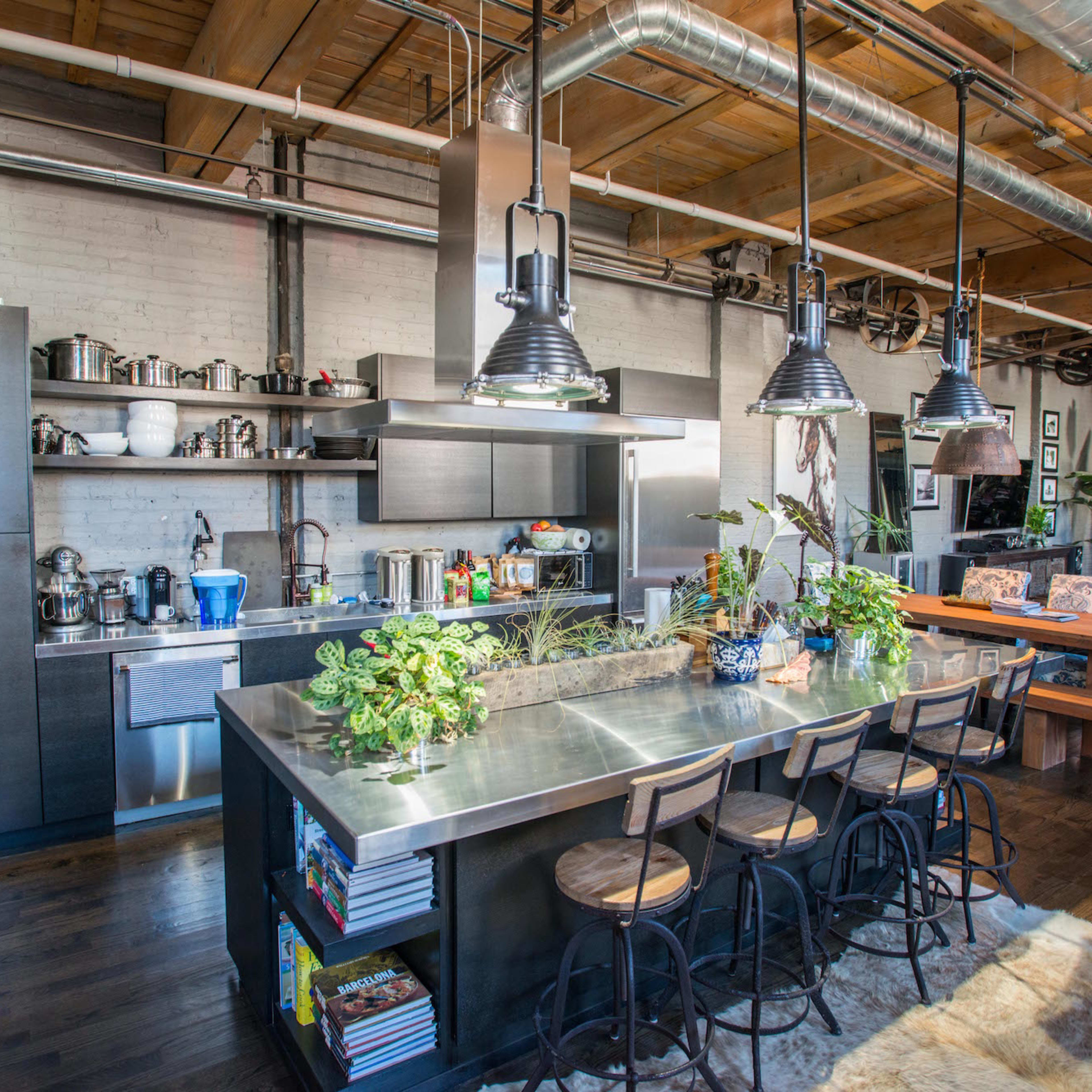 A modern kitchen featuring stainless steel appliances, a central island with bar stools, and wooden beams overhead.