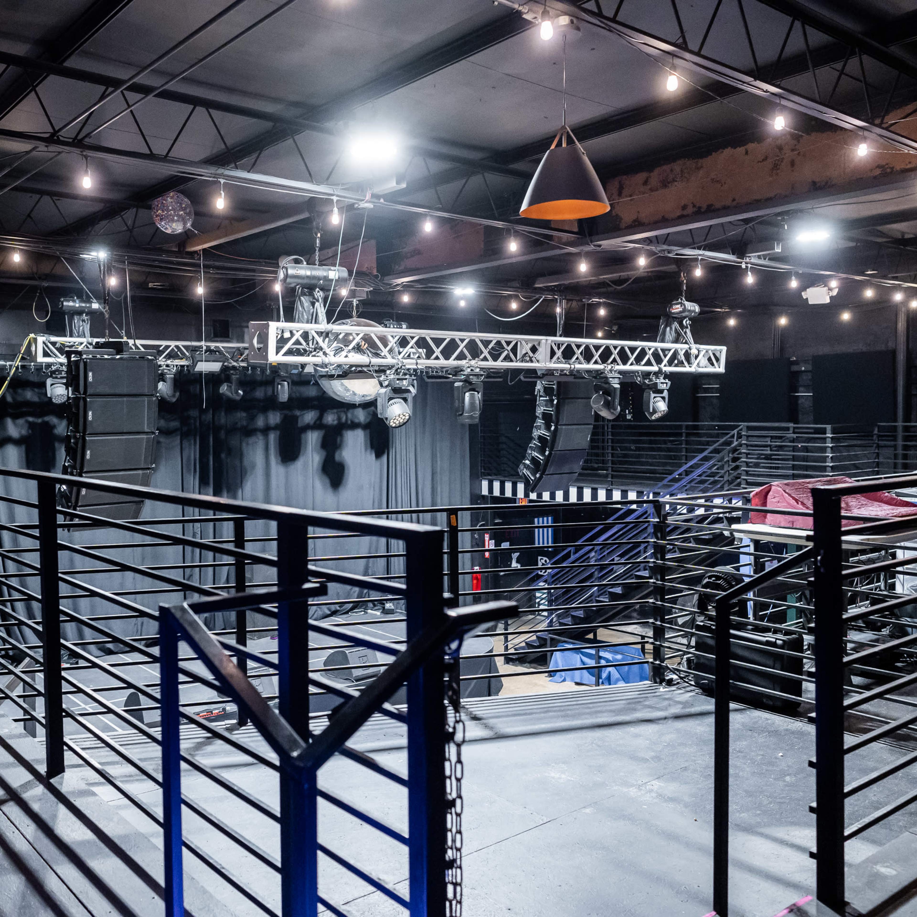 An empty indoor venue with metal railings, hanging lights, and suspended sound equipment.