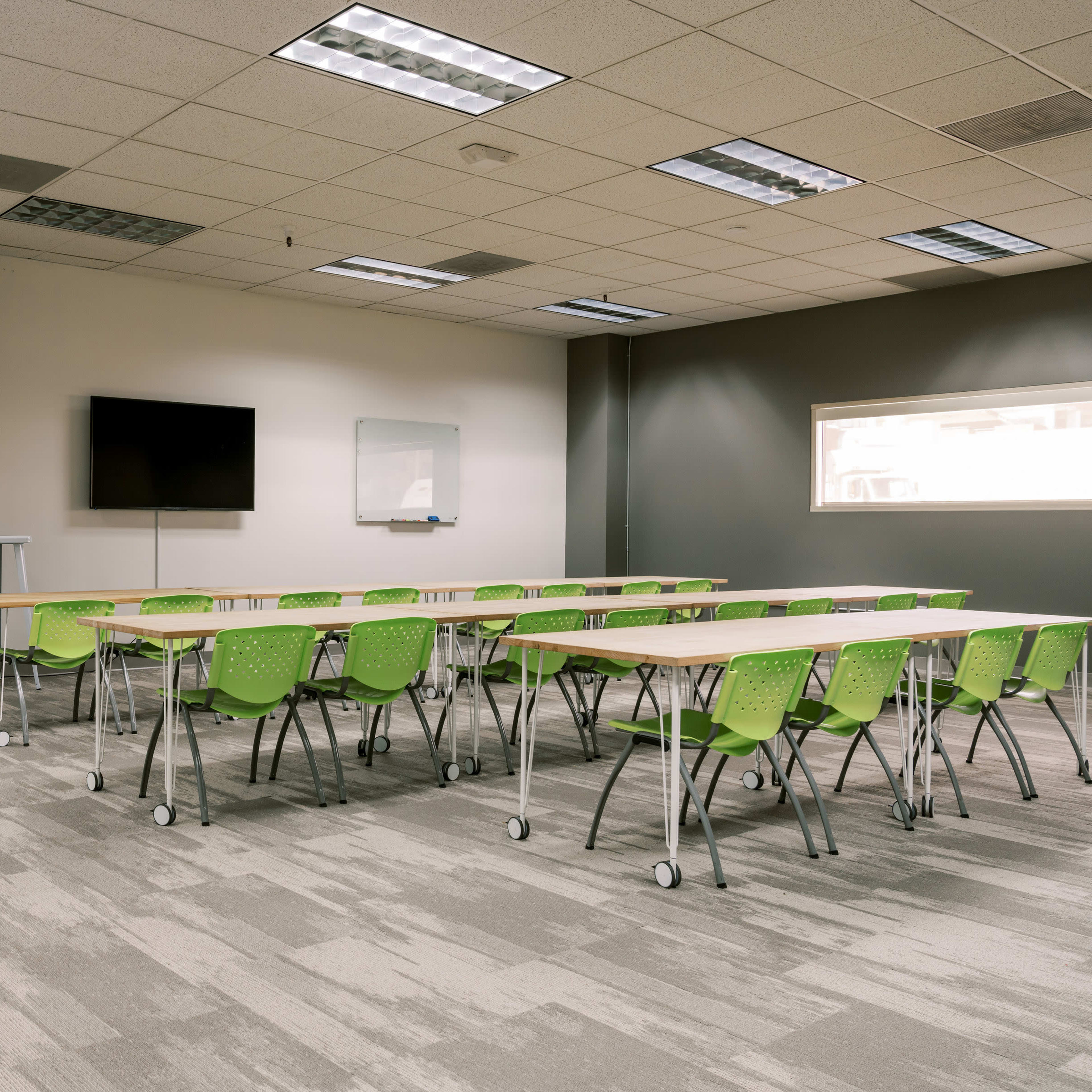 A classroom with green chairs and tables arranged in rows, featuring a wall with a quote and a television screen.