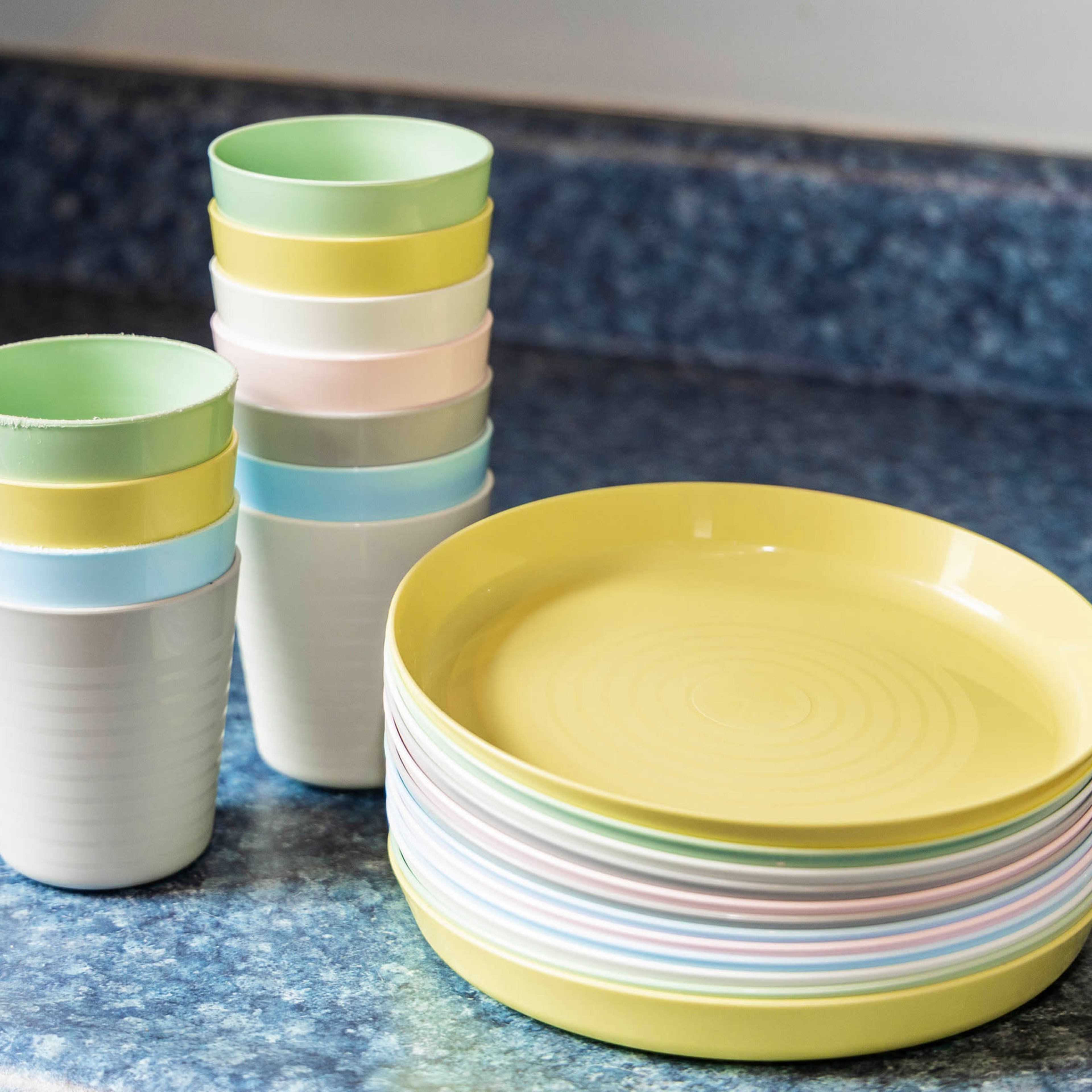 A stack of colorful cups and a stack of yellow plates are arranged on a blue countertop.