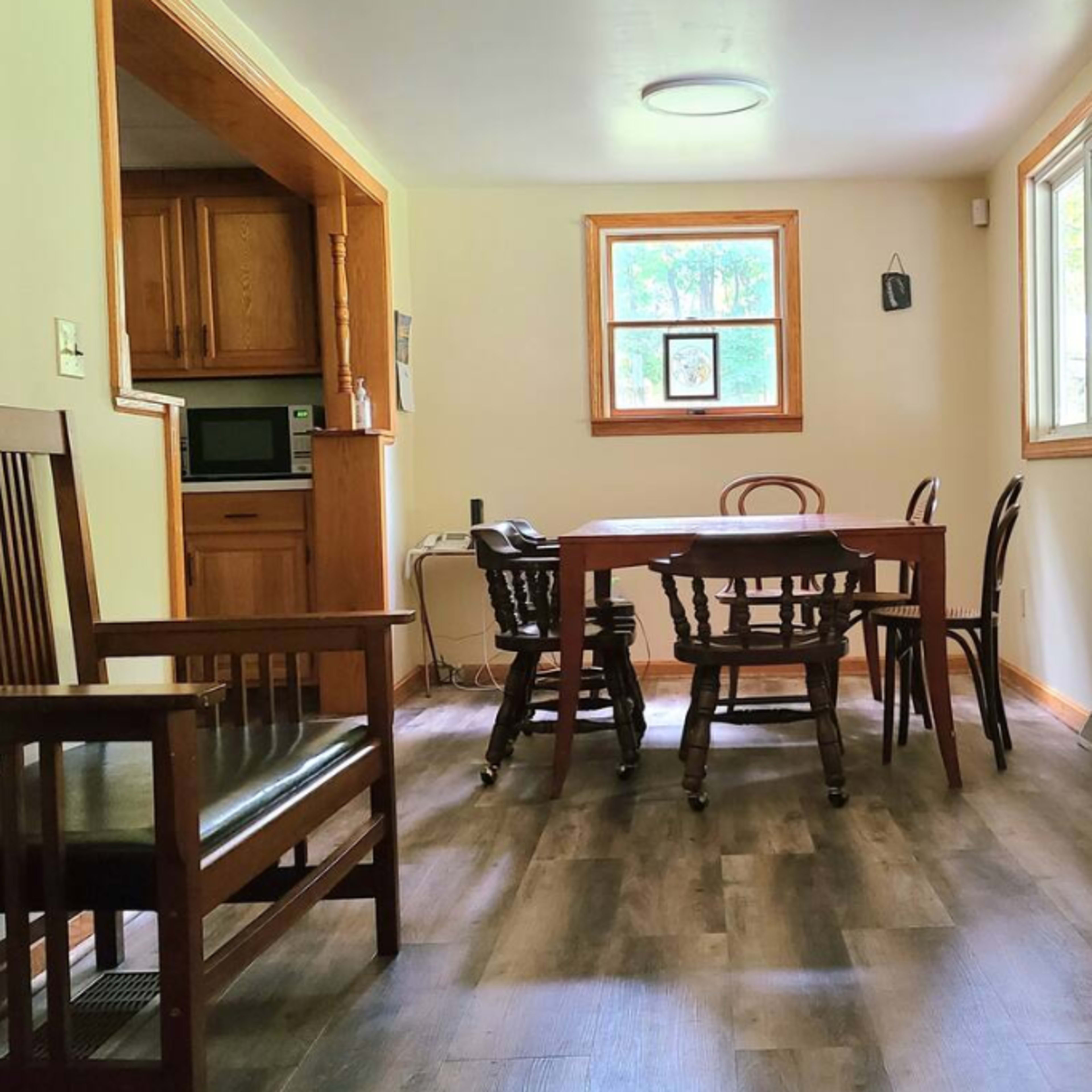 A kitchen-dining area with a wooden table surrounded by chairs, a bench, and a window letting in natural light.