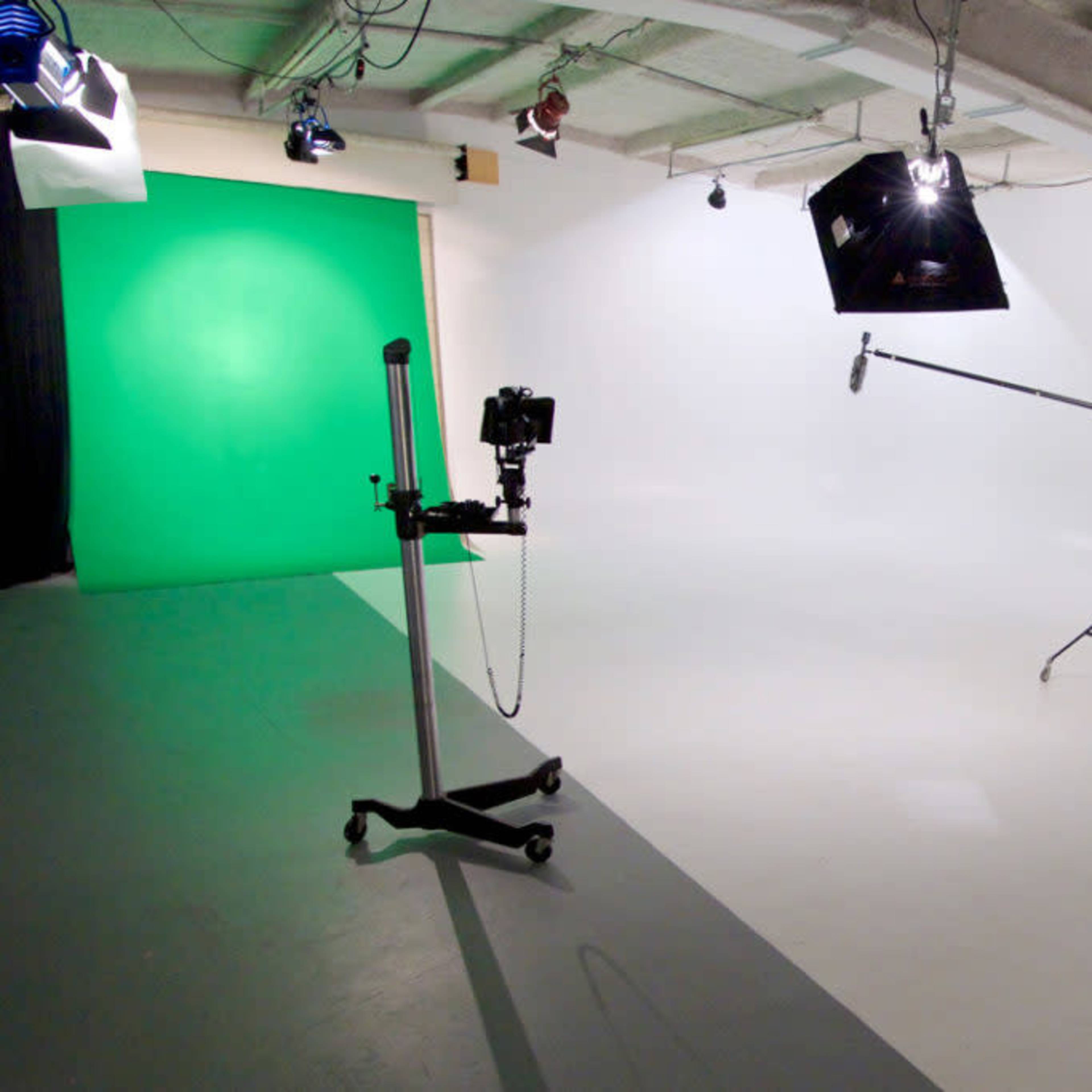 A photography studio with a green backdrop, lighting equipment, and a camera on a stand.