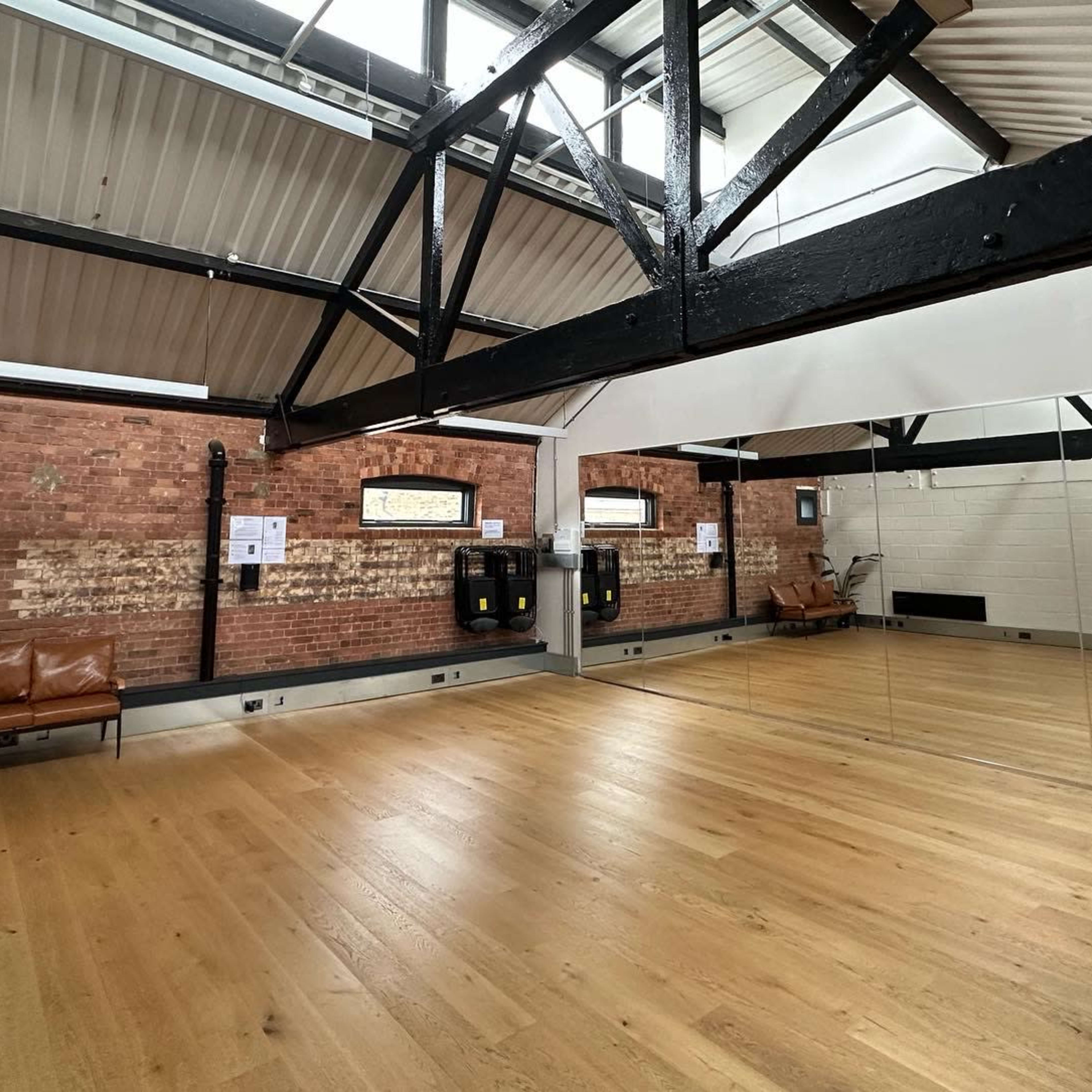 A spacious interior with wooden flooring, exposed brick walls, and large mirrors along one side.