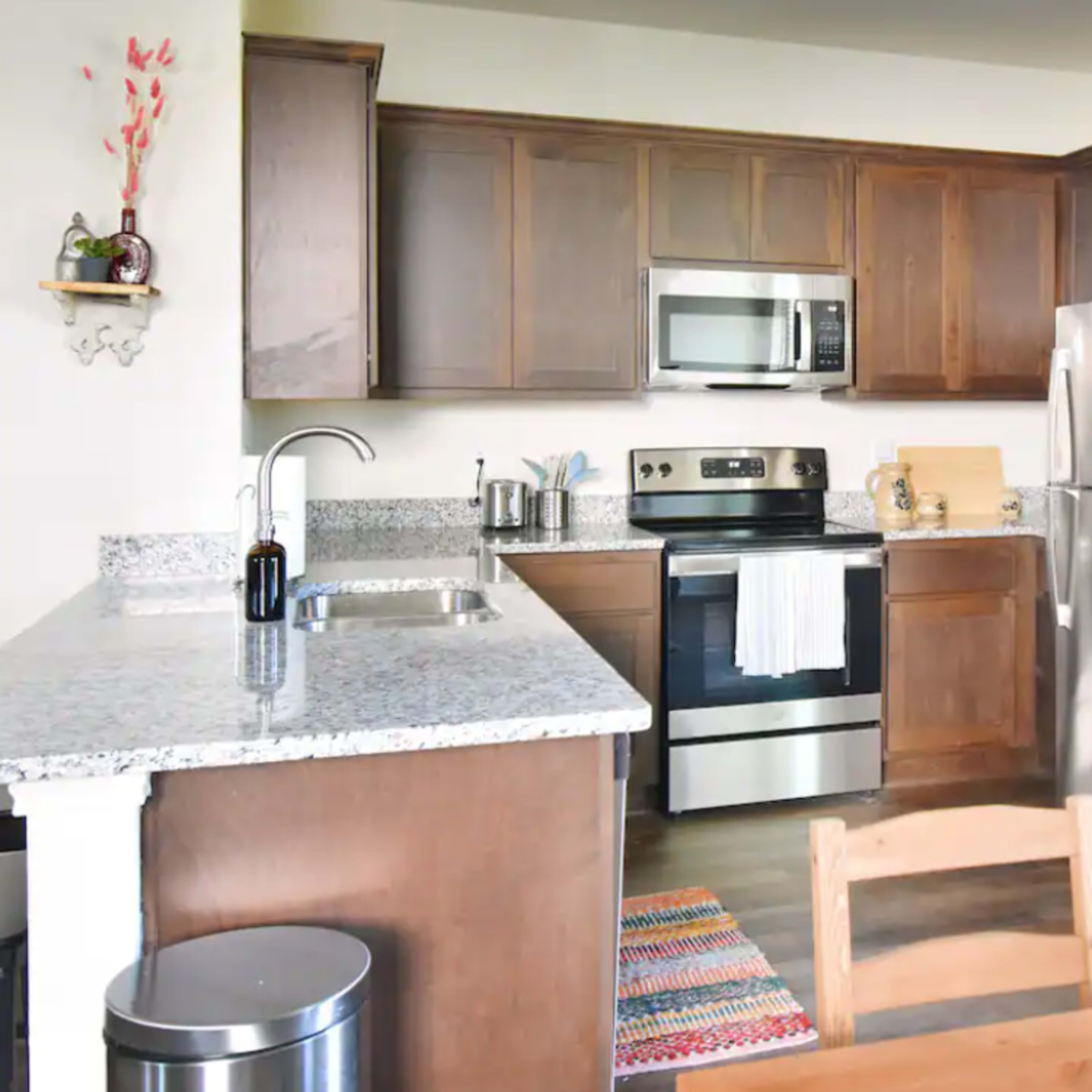 A modern kitchen with wooden cabinets, stainless steel appliances, and a dining table set near a flower vase.
