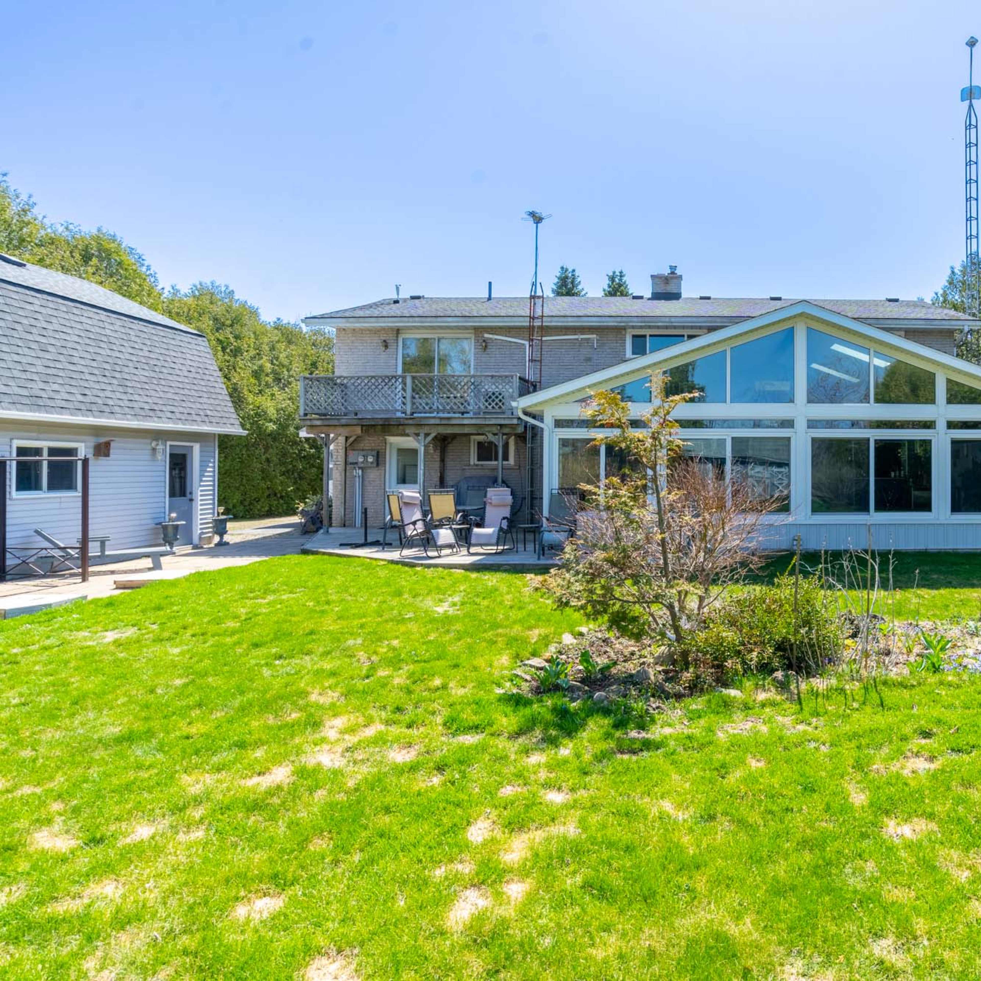 A two-story house with large windows and a deck overlooks a grassy yard, surrounded by trees.