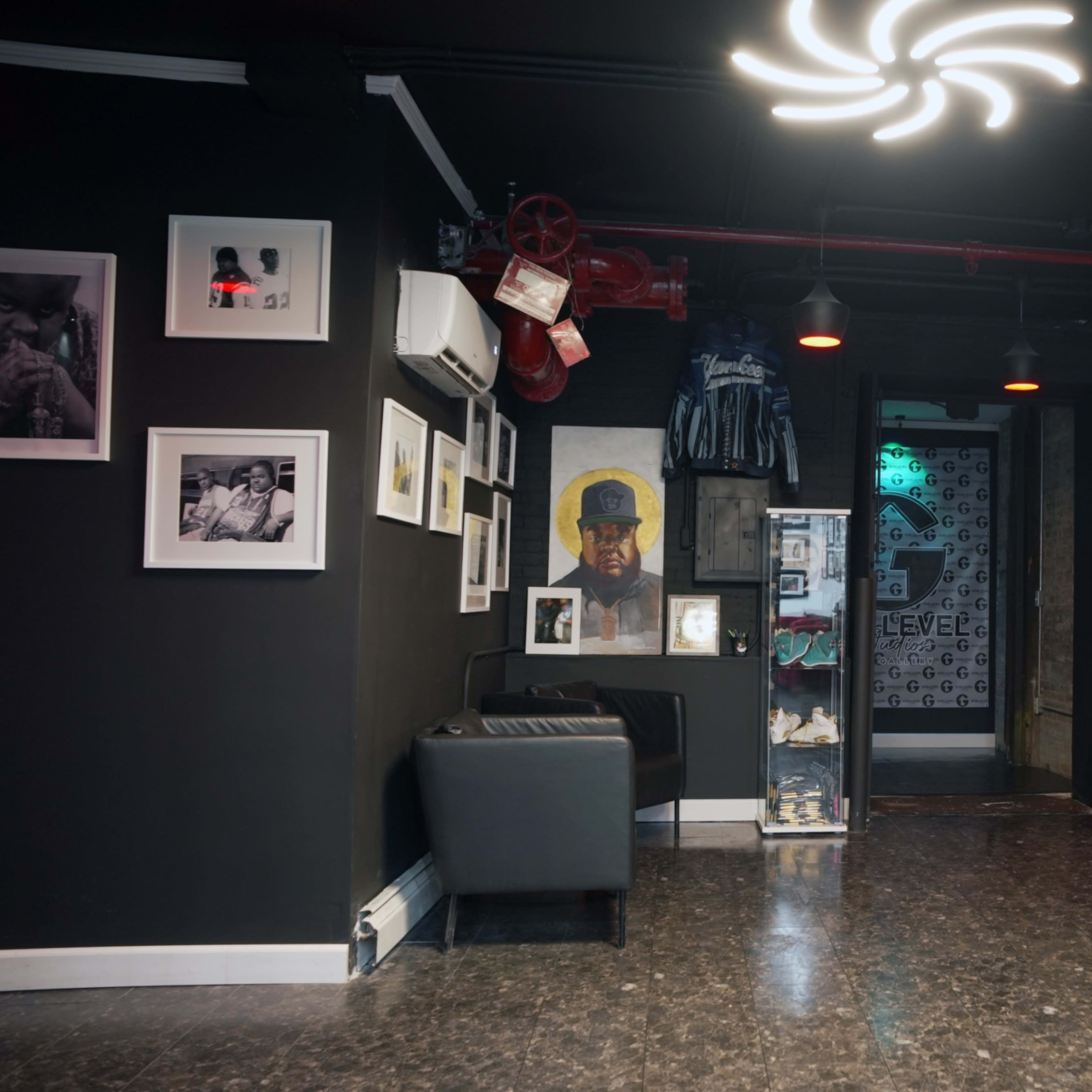 A modern interior space featuring black walls adorned with framed photographs and artwork, along with a mannequin dressed in red, and a seating area with a black chair.