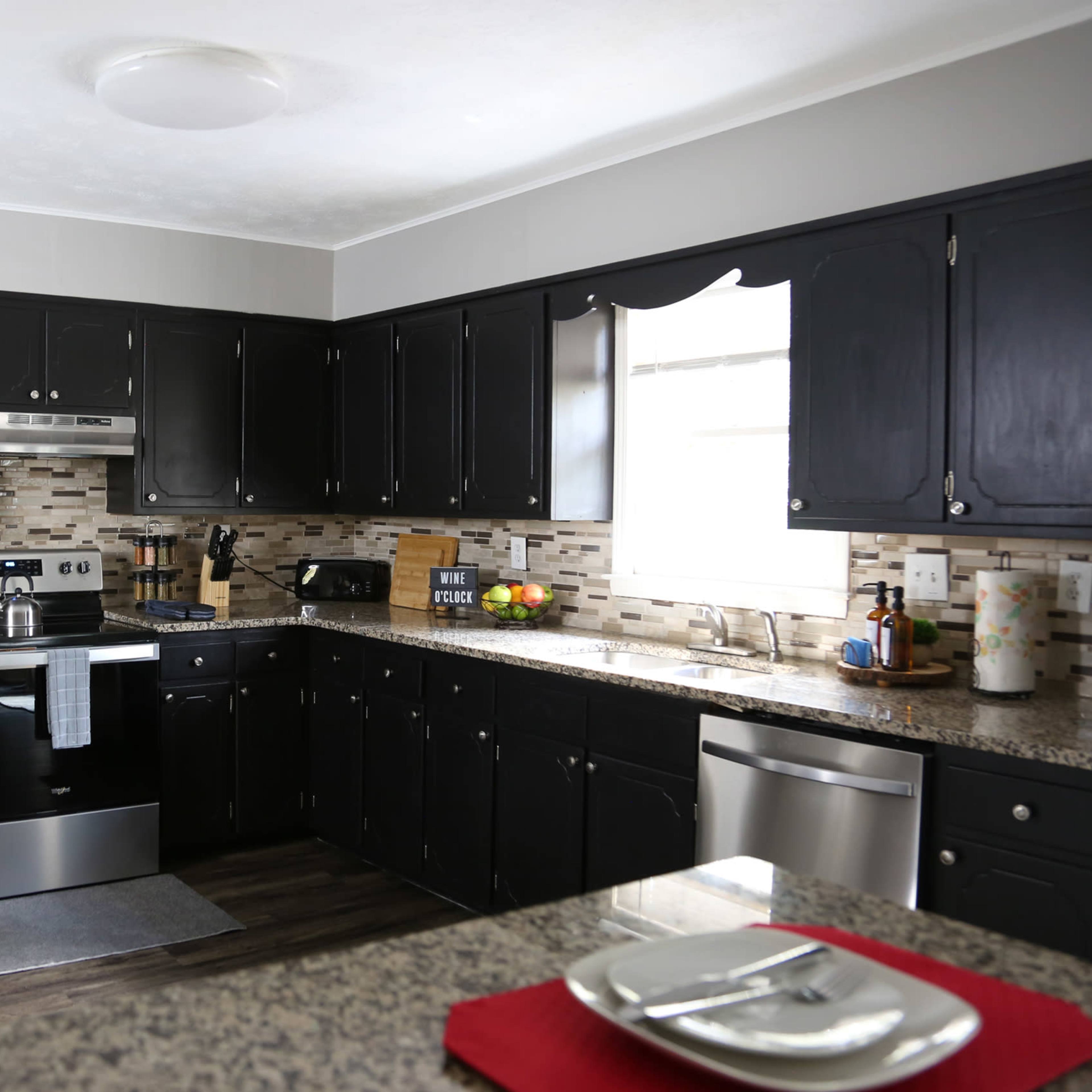 A modern kitchen features dark cabinets, stainless steel appliances, and a granite countertop with a view of a window.