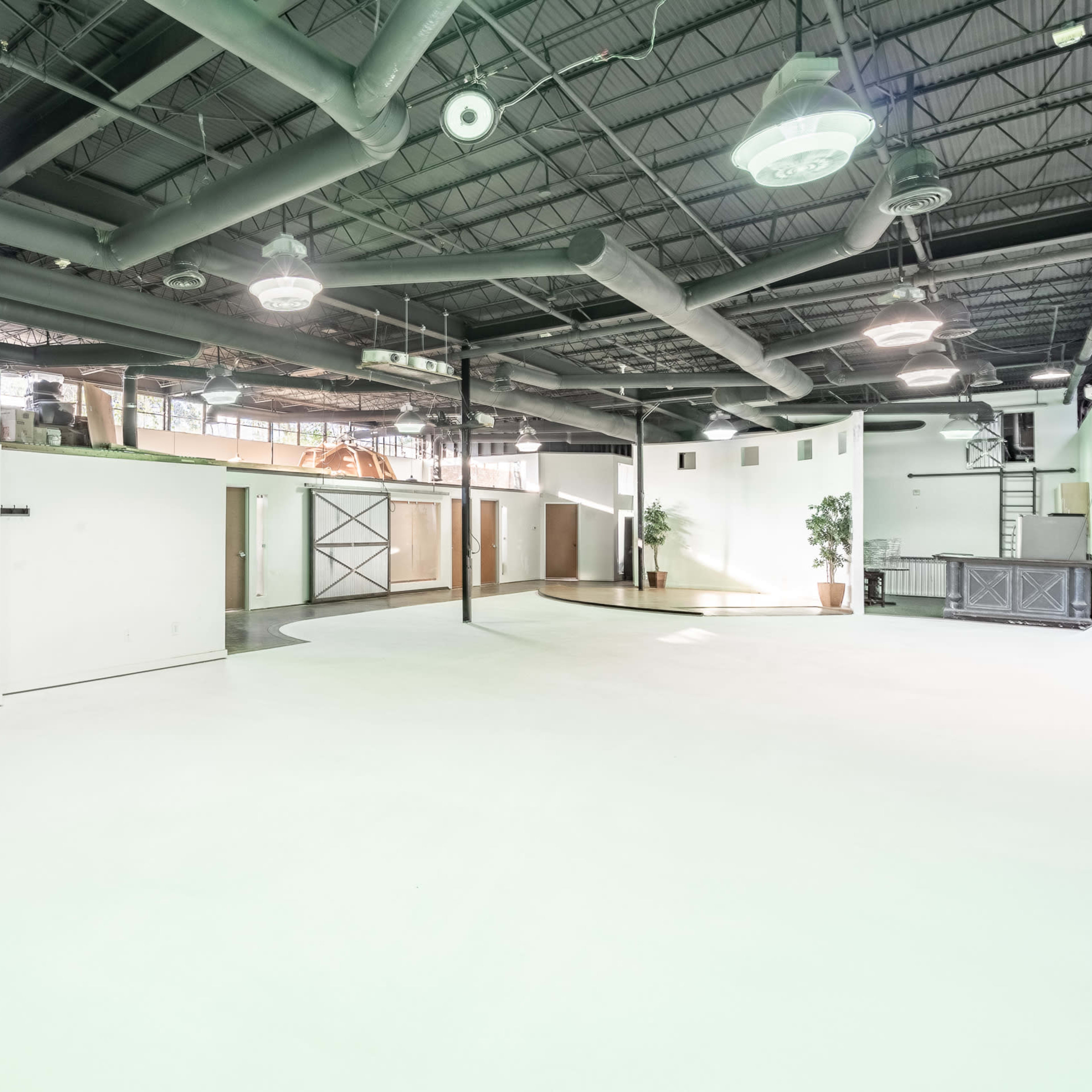 A spacious, well-lit industrial room with high ceilings, exposed ducts, and minimal furnishings.