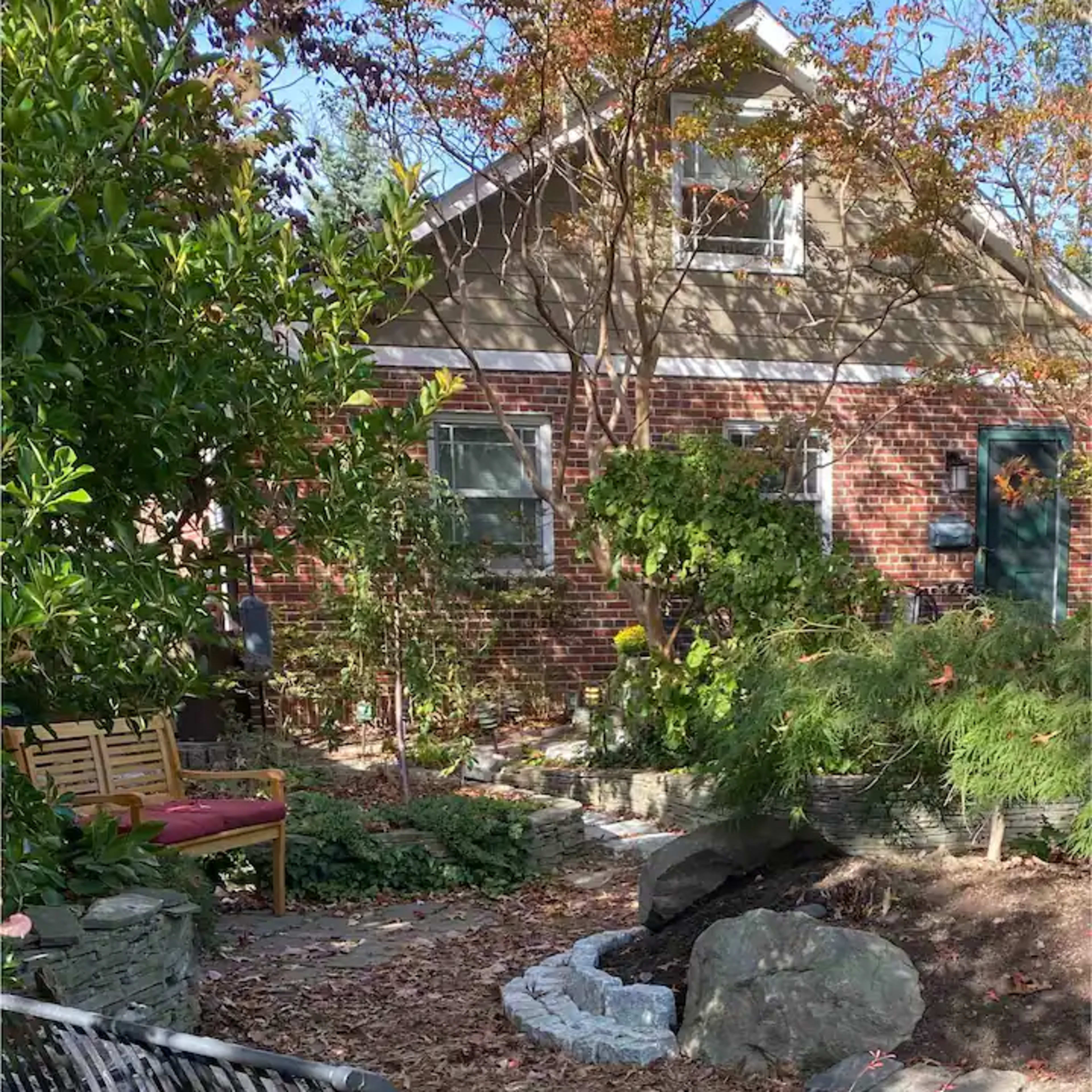 A well-tended garden with a wooden bench, rocks, and various plants in front of a brick house.