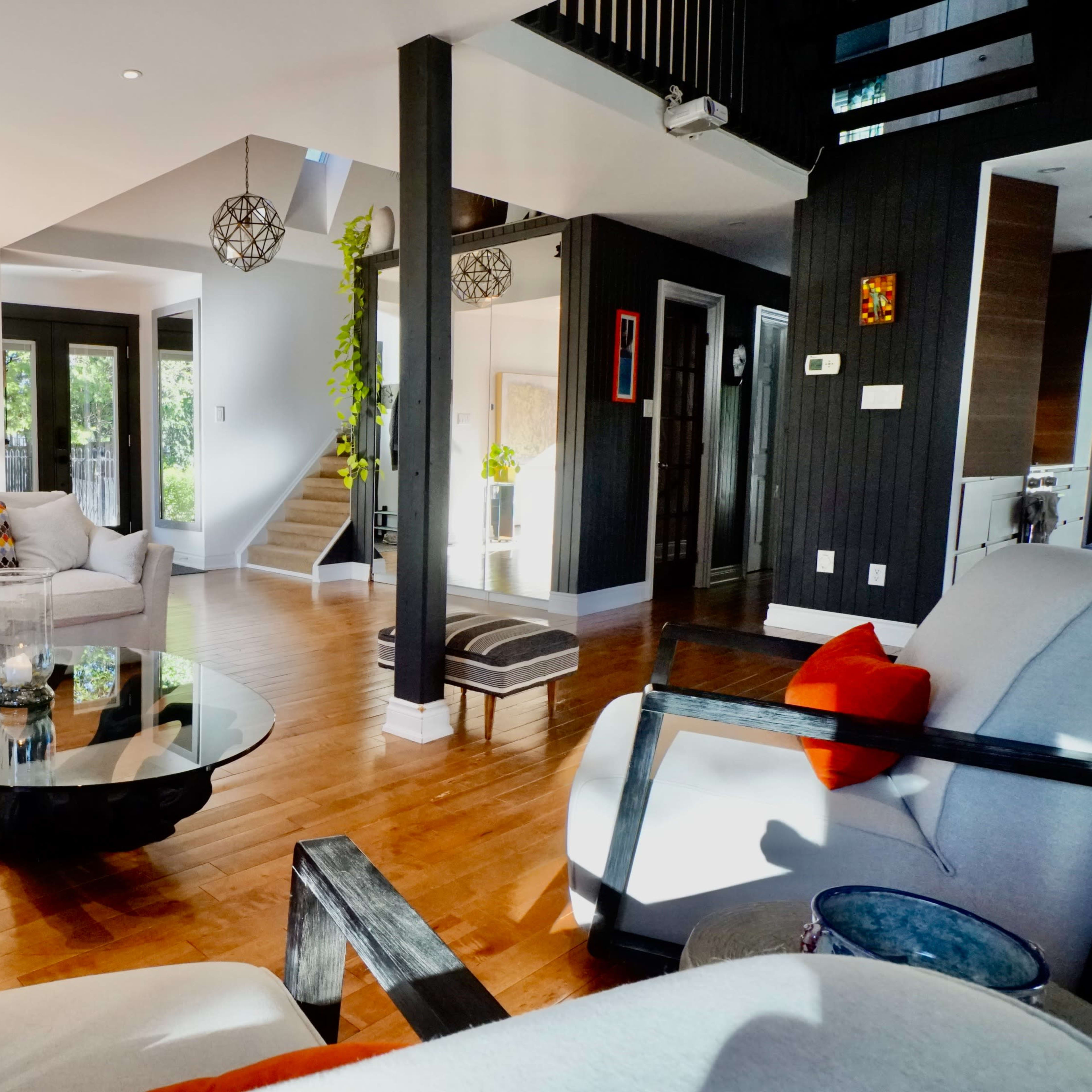 A spacious living room with wooden floors, modern furniture, and large windows letting in natural light.