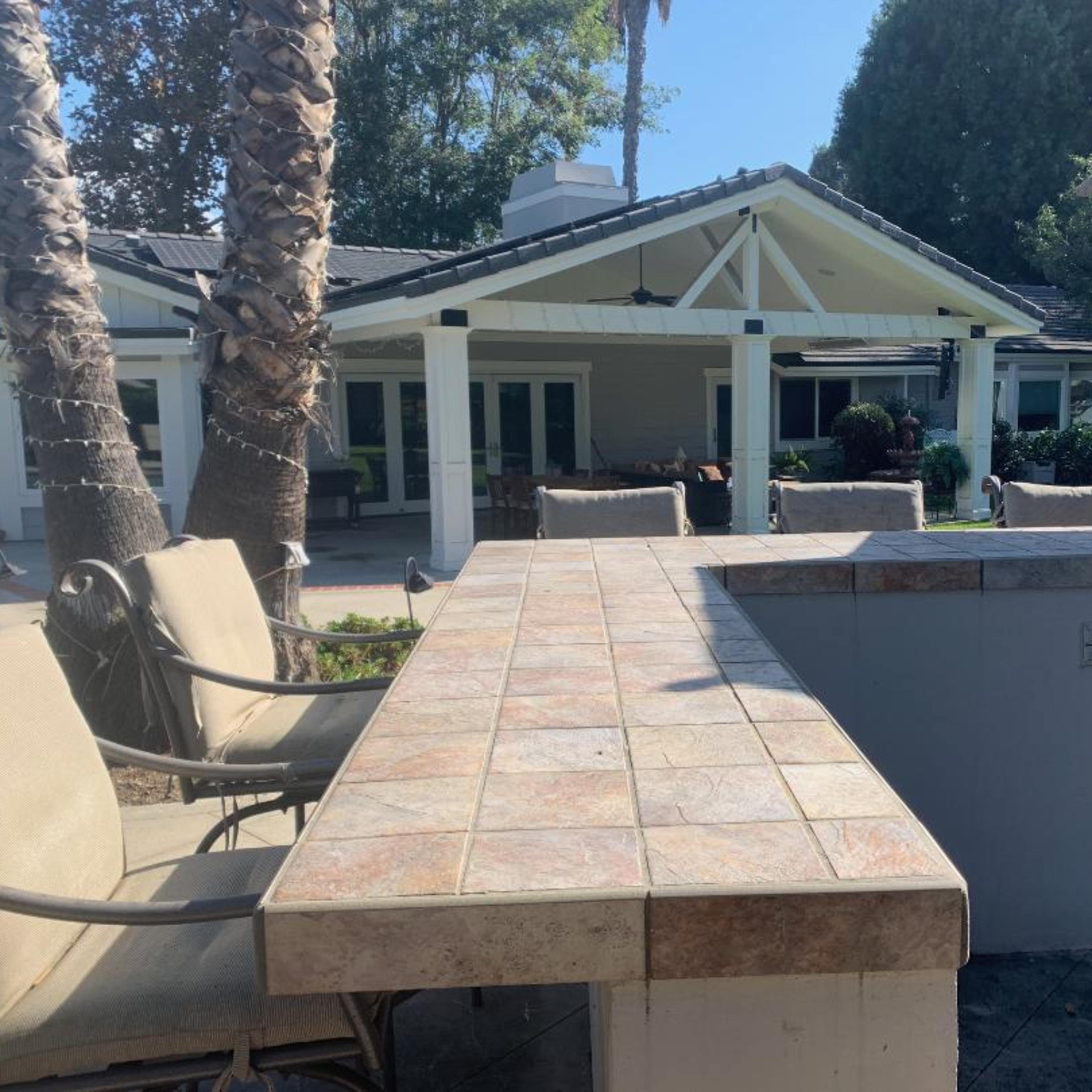 An outdoor patio area with a tiled bar, seating, and a view of a house surrounded by palm trees.