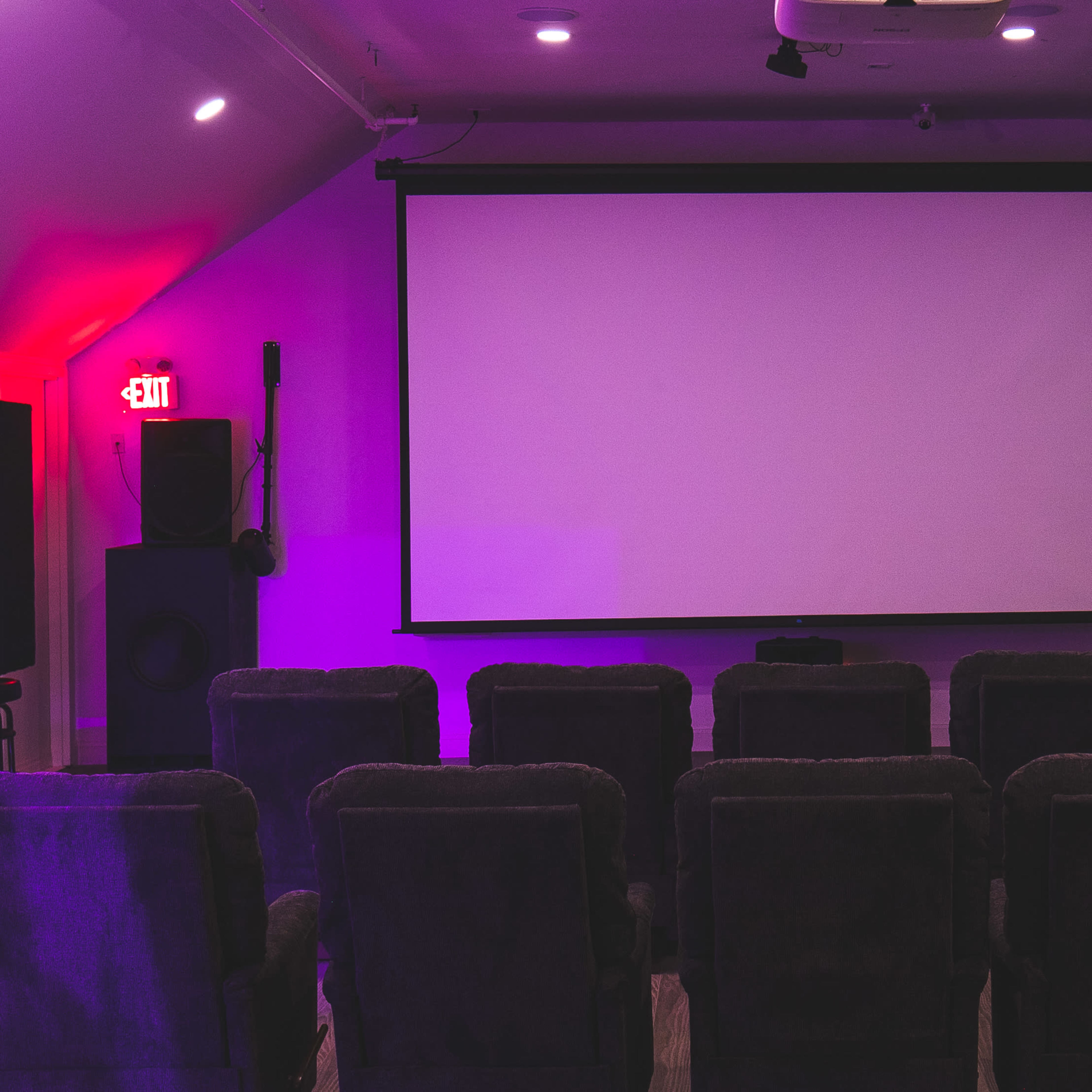 A small home theater with a blank projection screen and rows of dark upholstered chairs facing it.