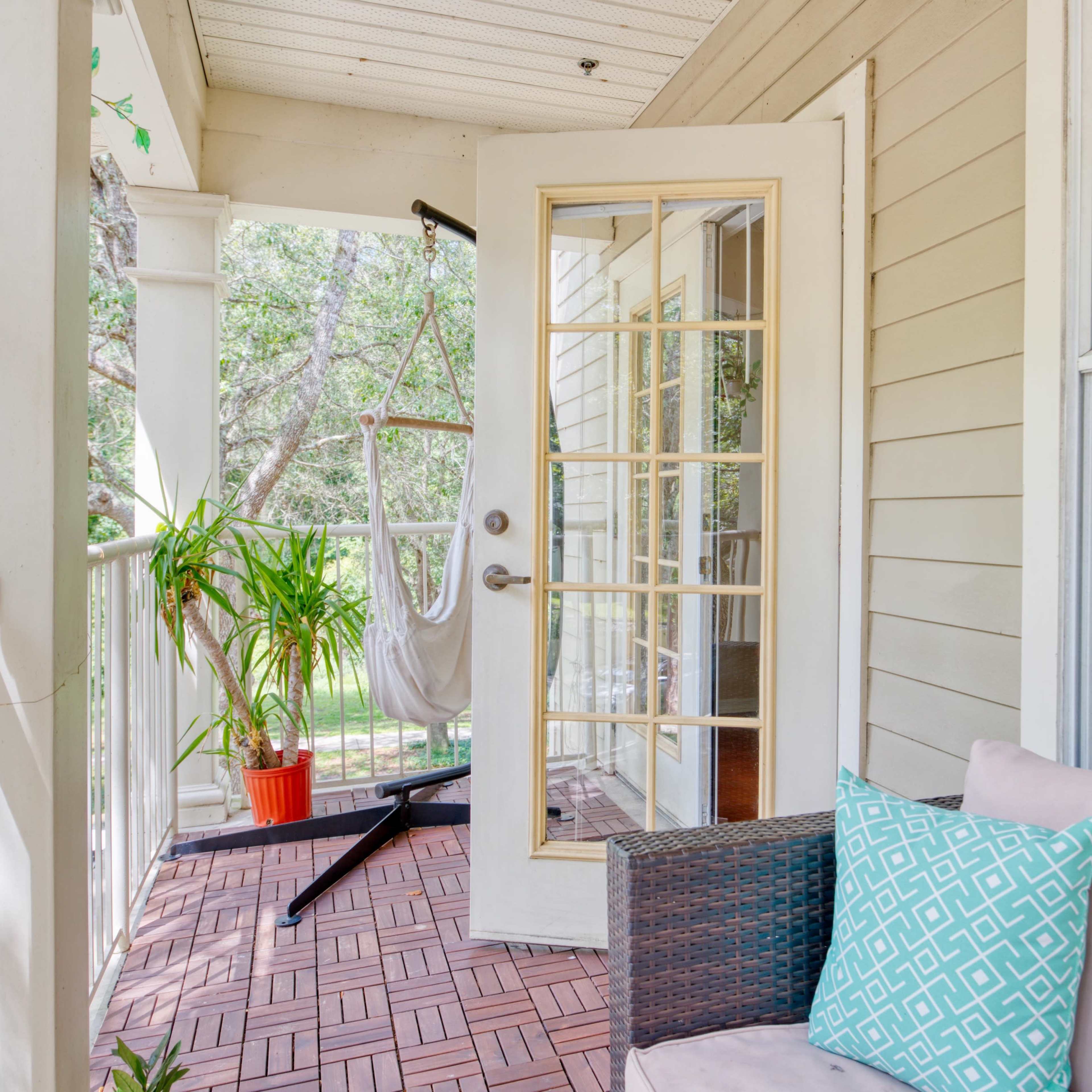 A porch area with a swinging chair, a potted plant, and a couch adorned with a decorative pillow, framed by a glass door.