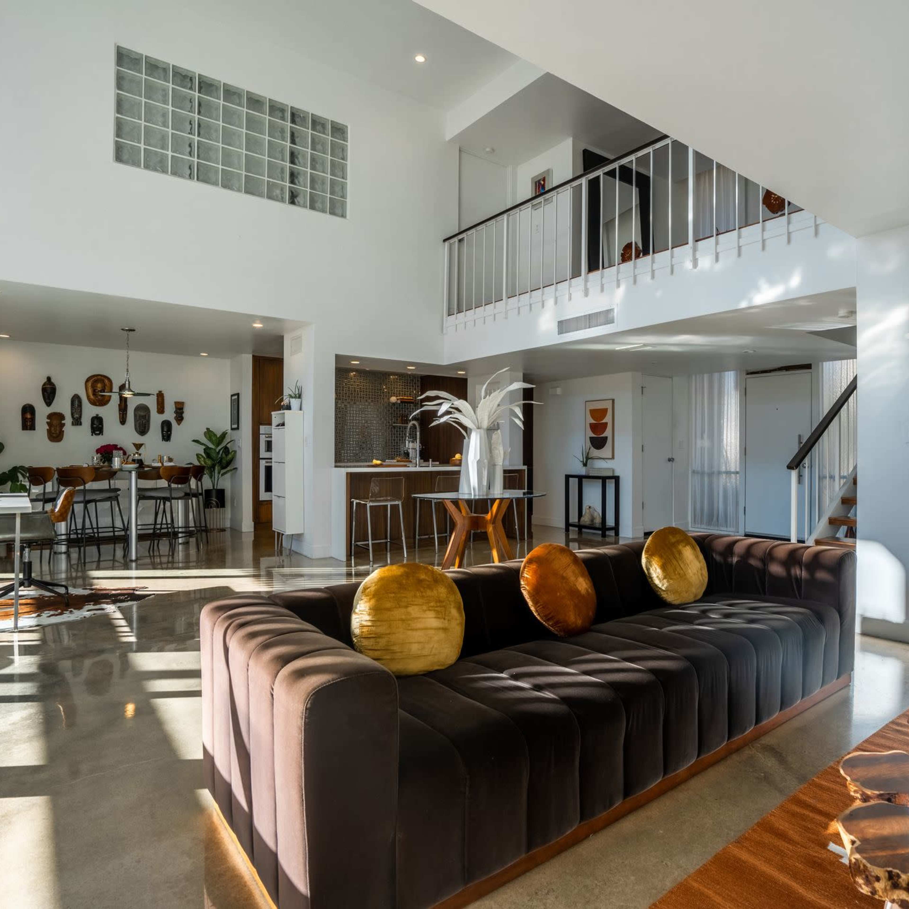 A modern living room with a dark sofa, wooden coffee table, and an open layout that connects to a dining area and kitchen.