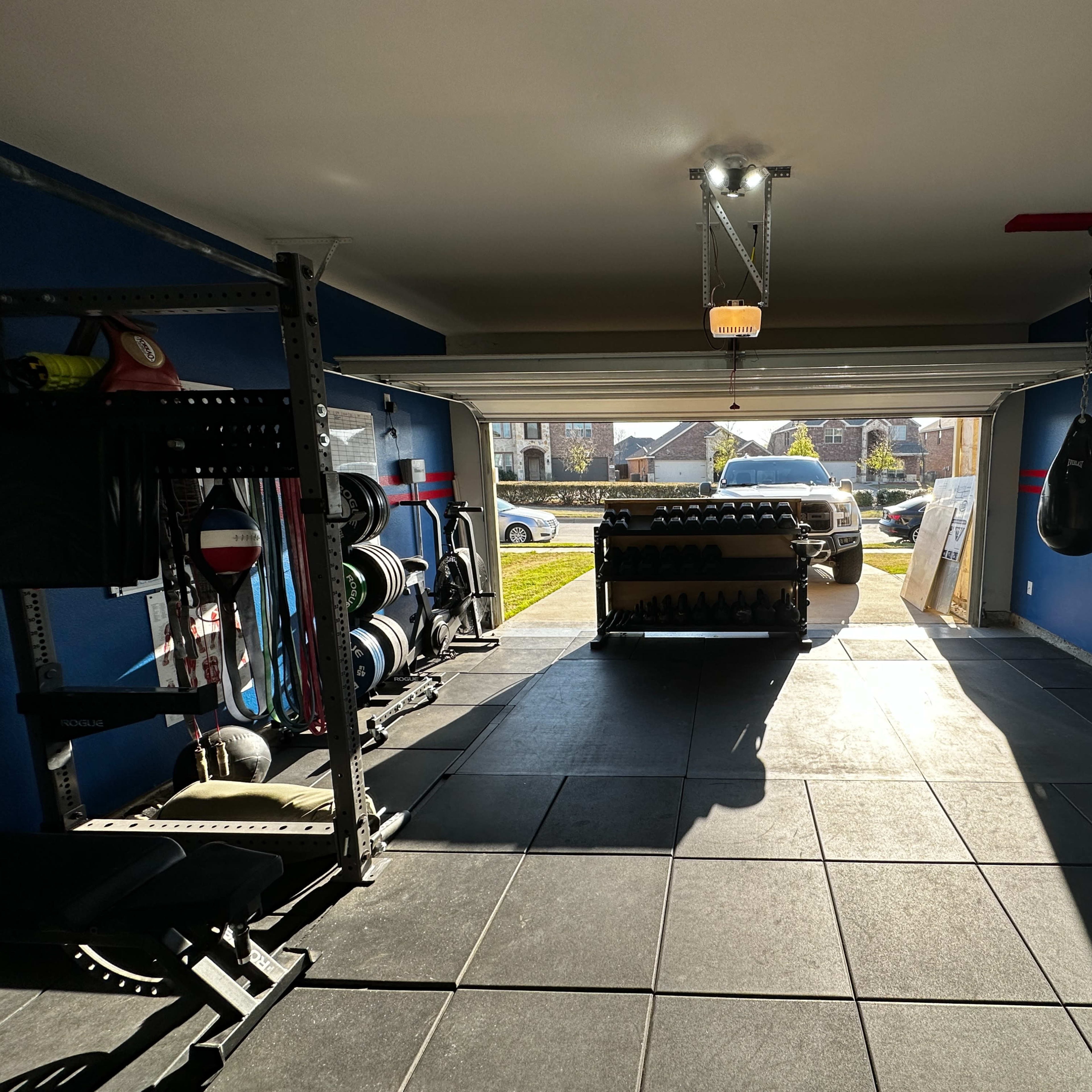 A garage gym equipped with weights, a punching bag, and large windows allowing natural light to enter.