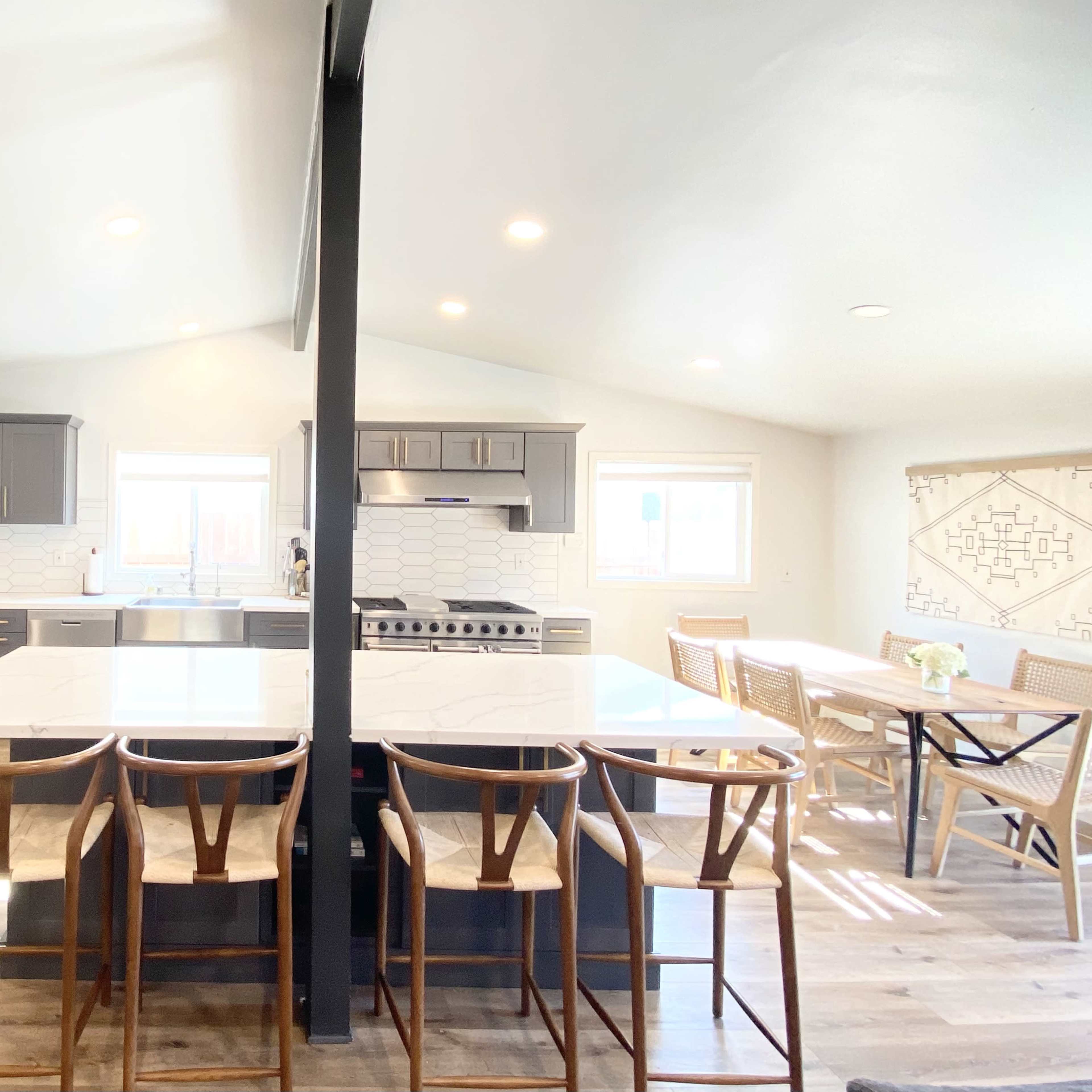 A modern kitchen features gray cabinets, stainless steel appliances, a large island with seating, and a dining area with a table and chairs.