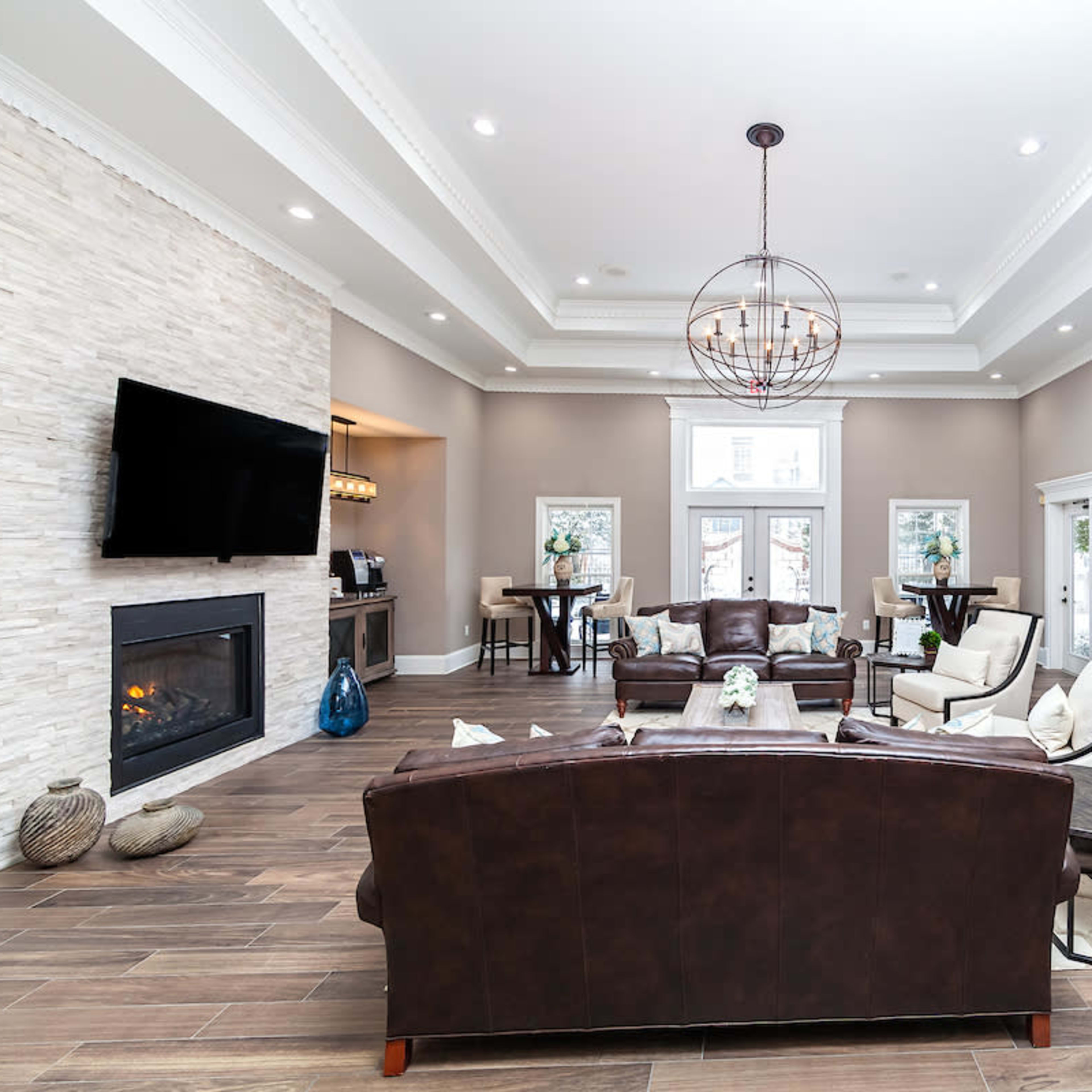 The spacious living area features a leather sofa, a stone fireplace, and a large television, with modern furnishings and an open kitchen visible in the background.
