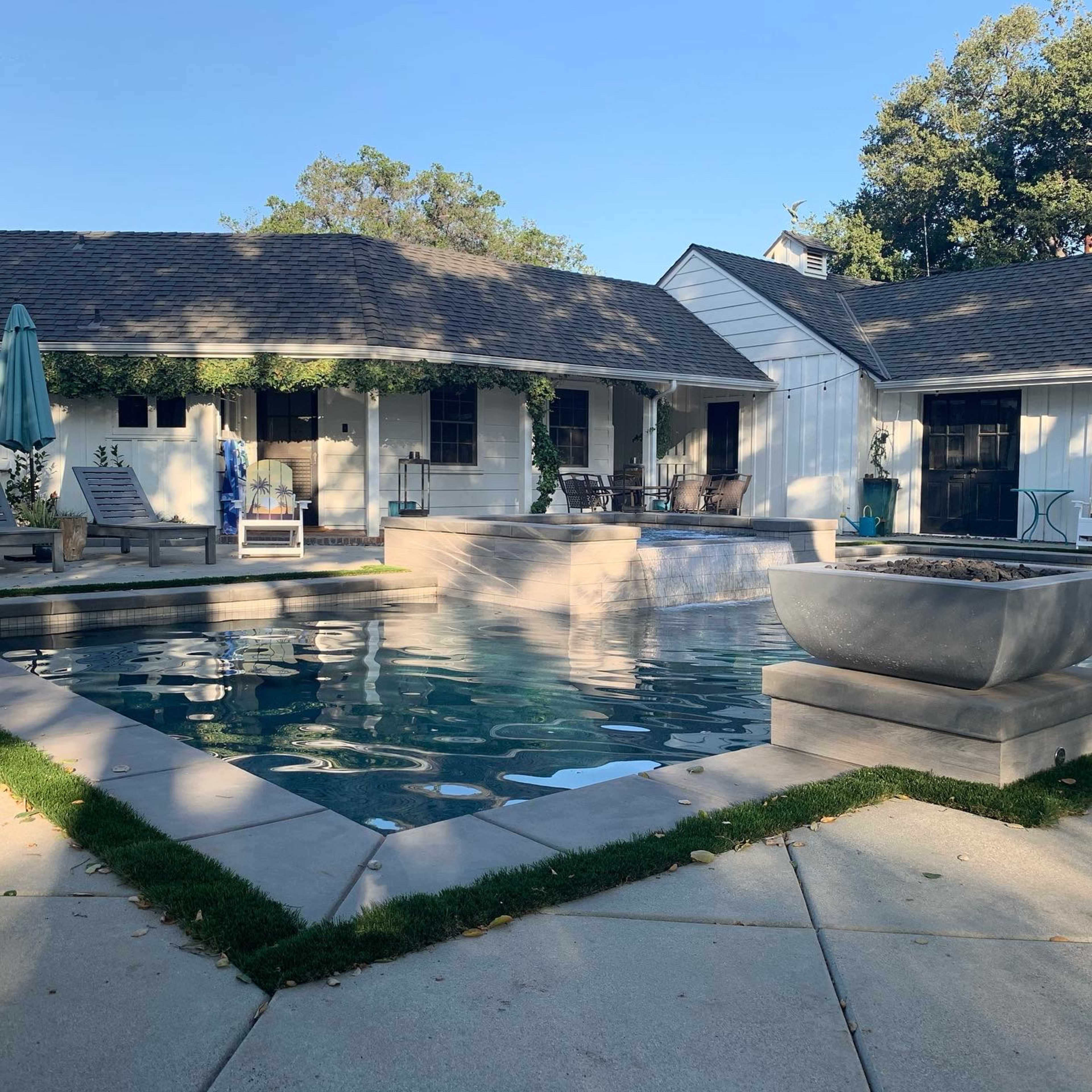 The scene features a backyard pool area surrounded by a patio and a single-story house.